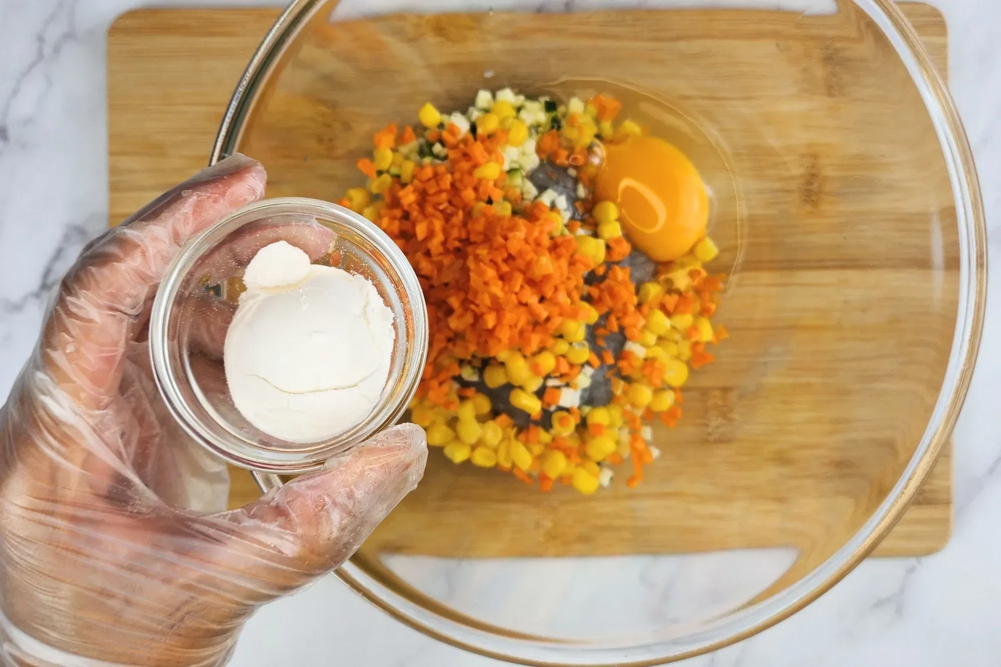 A hand is holding a bowl of flour above a mixing bowl.