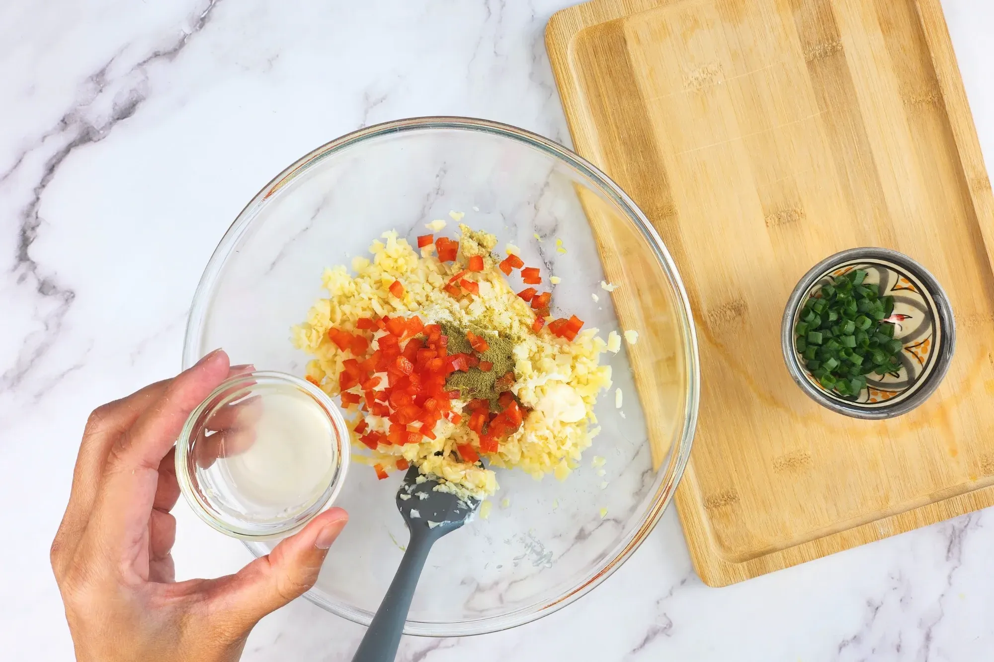 A hand is holding a bowl of lemon juice above the mixing bowl.