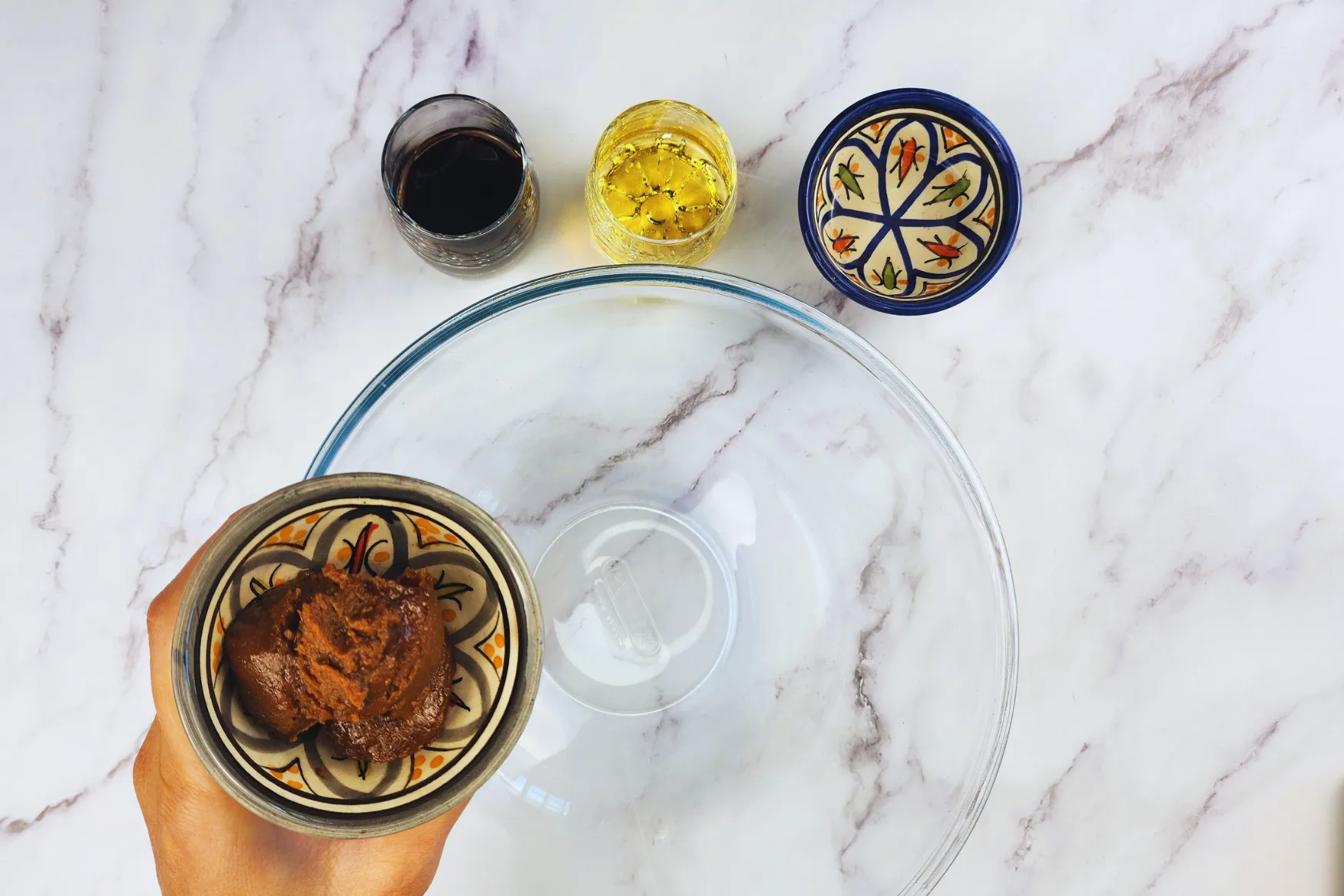 A hand is holding a bowl of miso paste above the mixing bowl.