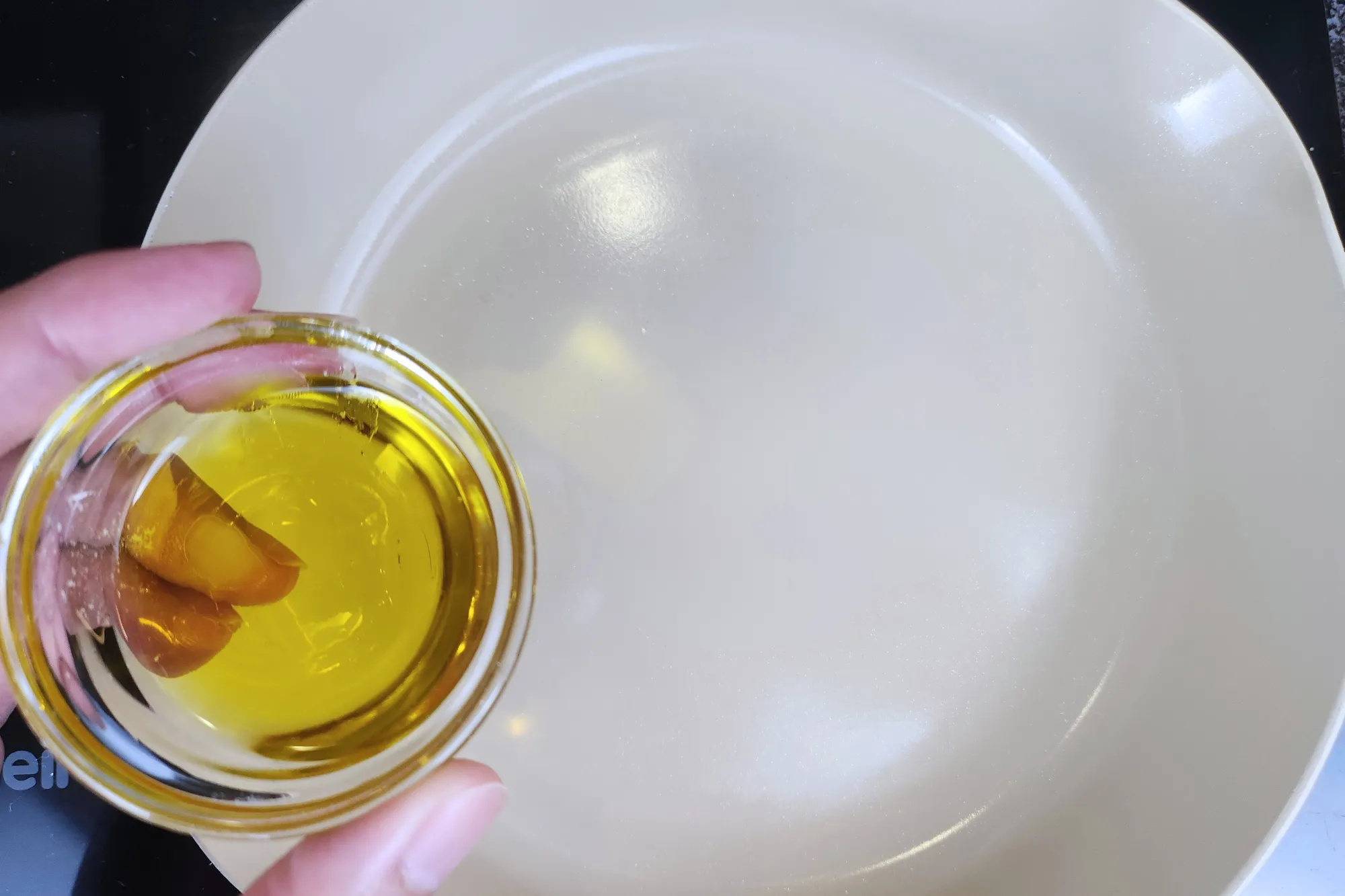 A hand is holding a bowl of oil above a pan