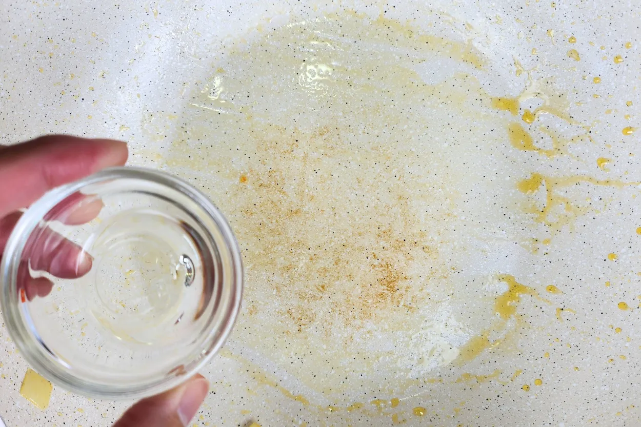 A hand is holding a bowl of oil above an used wok.