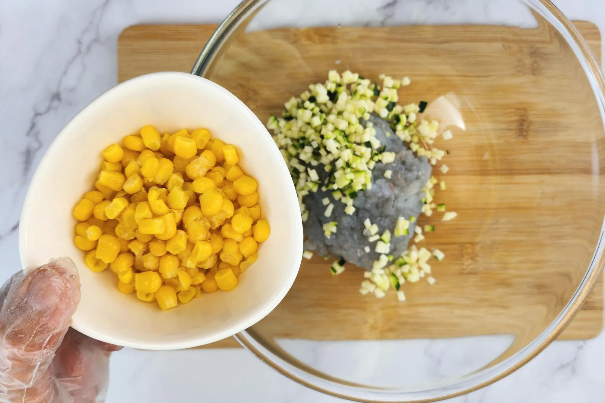 A hand is holding a bowl of orn above a mixing bowl