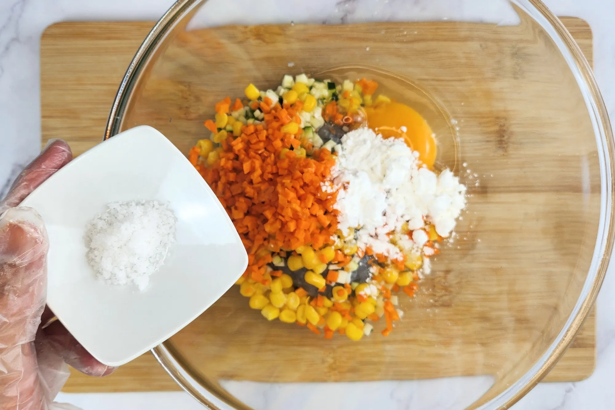 A hand is holding a bowl of salt above a mixing bowl.