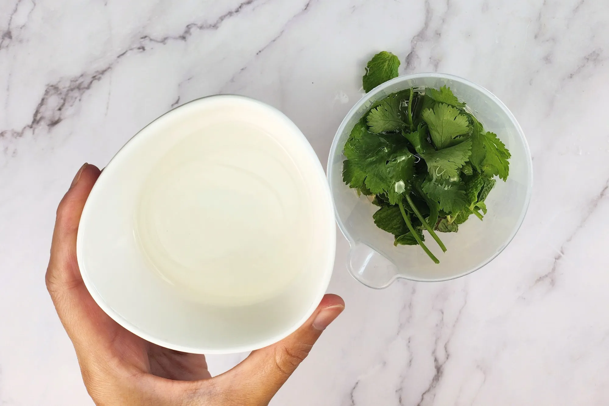 A hand is holding a bowl of vinegar is above a mixing jar.