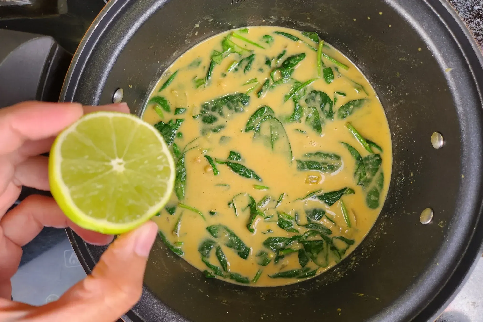 A hand is holding a half of lime above a pot