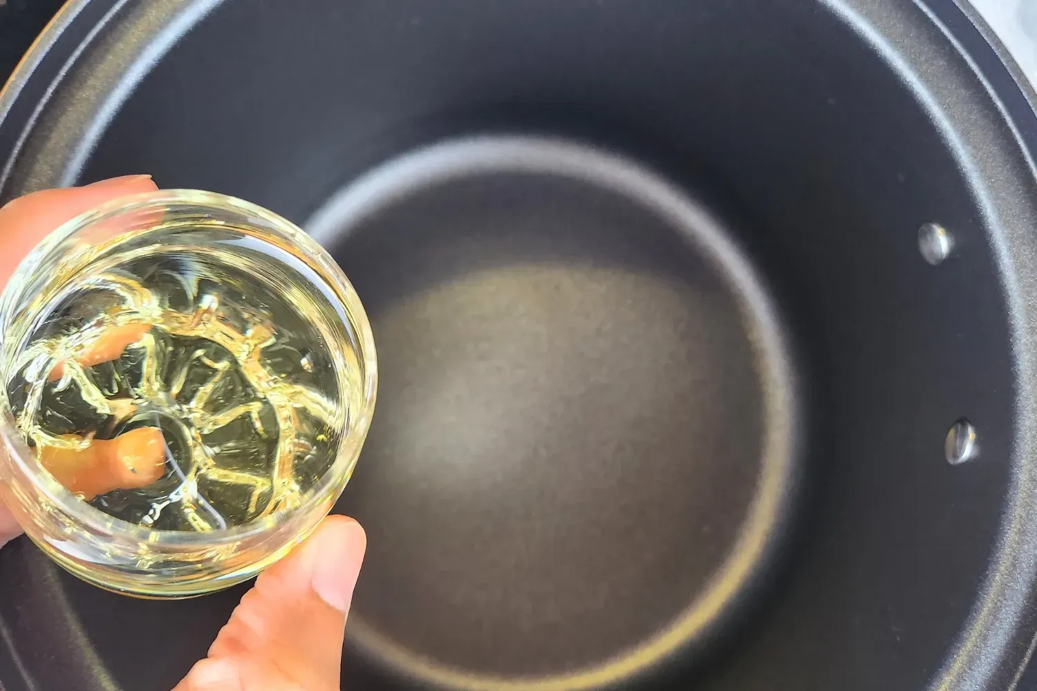 A hand is holding a small bowl of cooking oil.