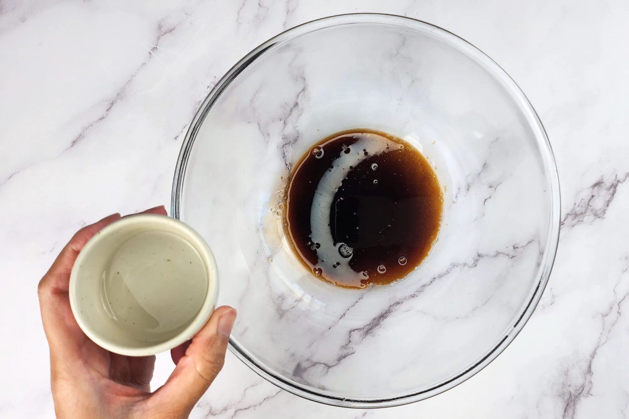 A hand is holding a small bowl of sake above a mixing bowl.