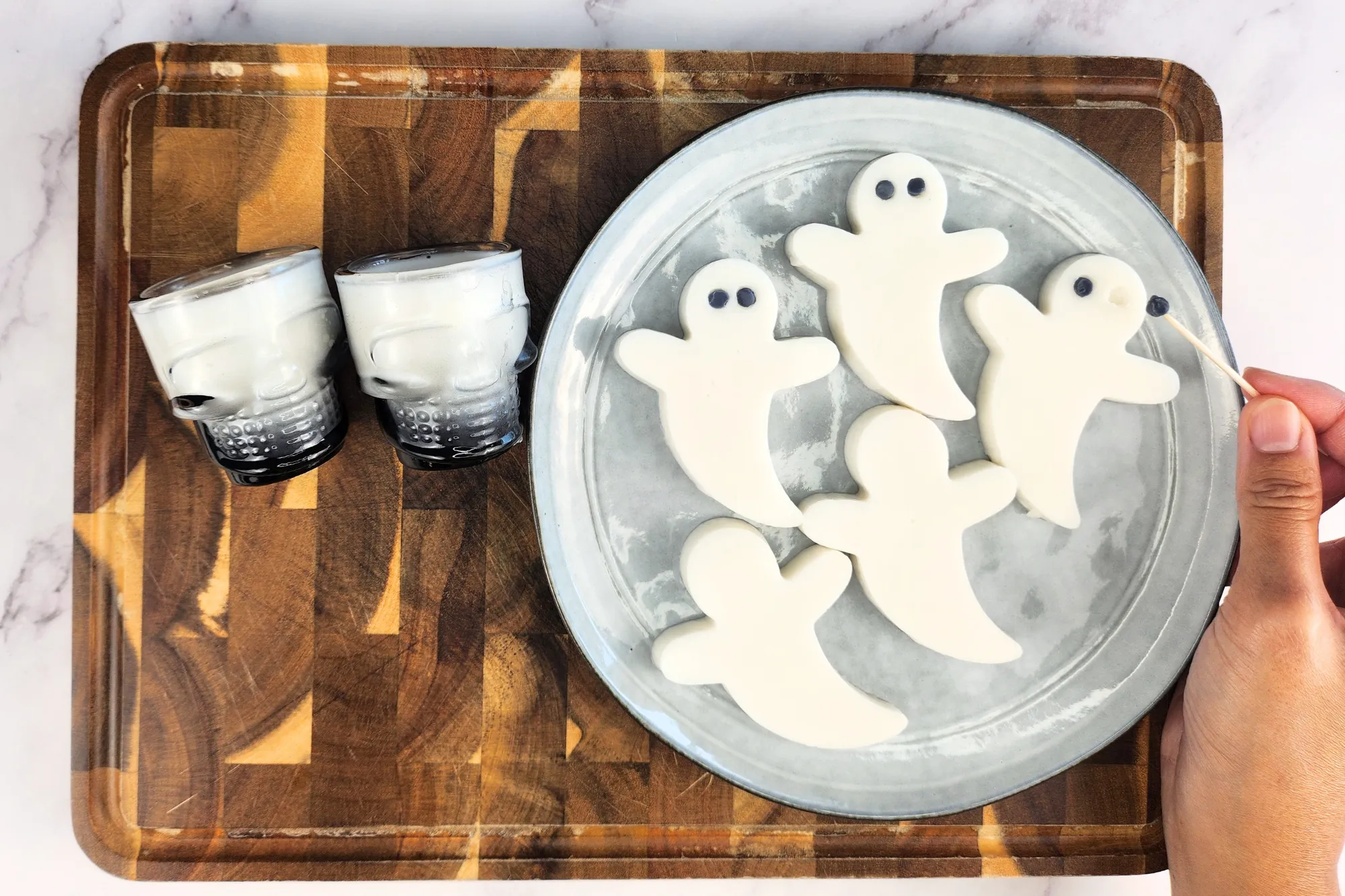 A hand is holding a toothpick to put black eyes on white ghost jelly