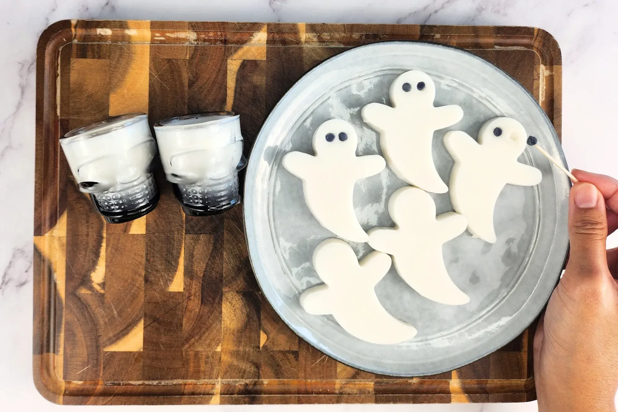 A hand is holding a toothpick to put black eyes on white ghost jelly