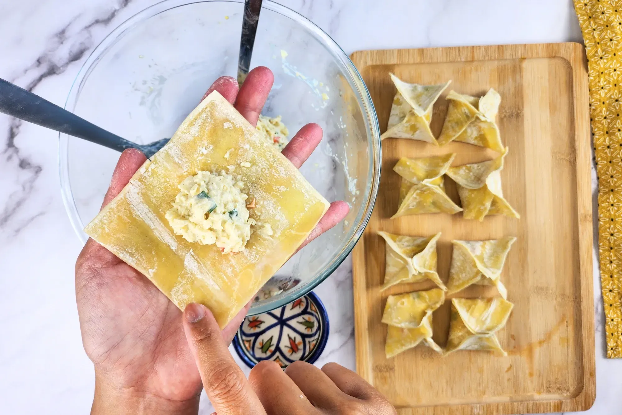 A hand is holding wonton wrapper with the filling and wet the edge of wonton wrapper.