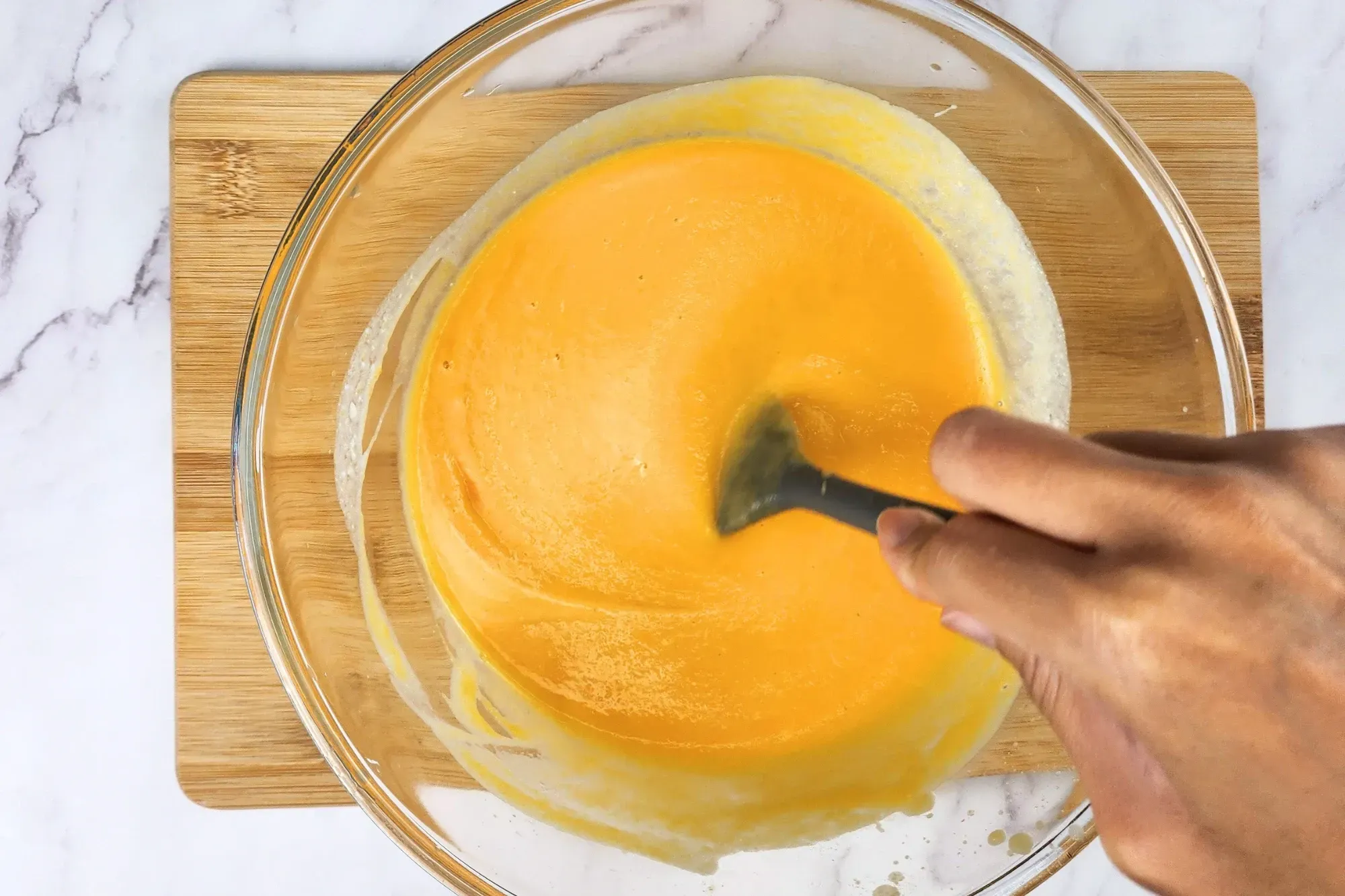 A hand is mixing pumpkin puree in a mixing bowl.