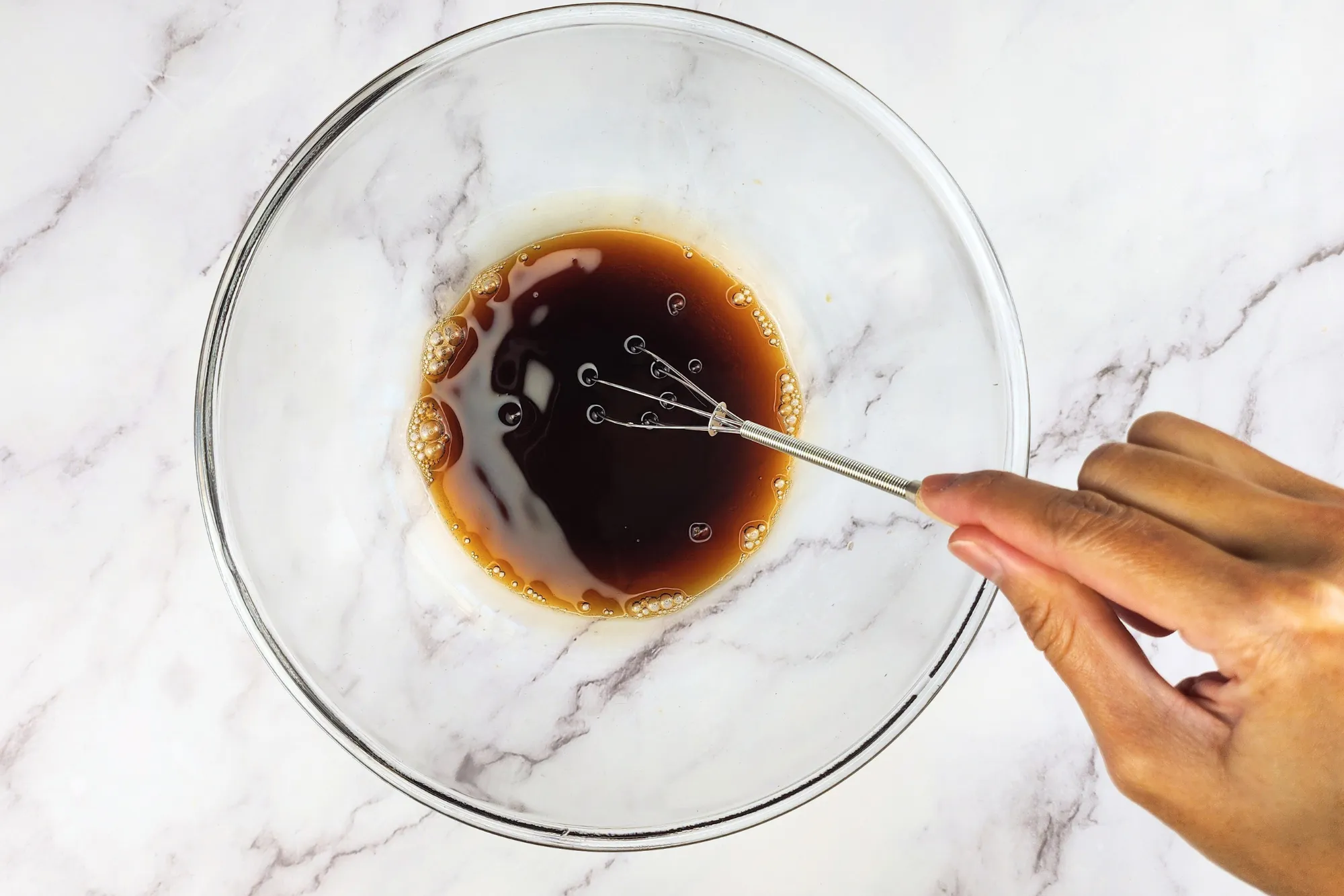 A hand is mixing sauce in a glass bowl.
