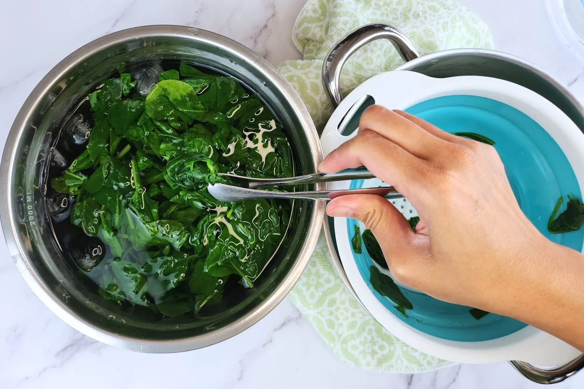 A hand putting cooked spinach in water bowl