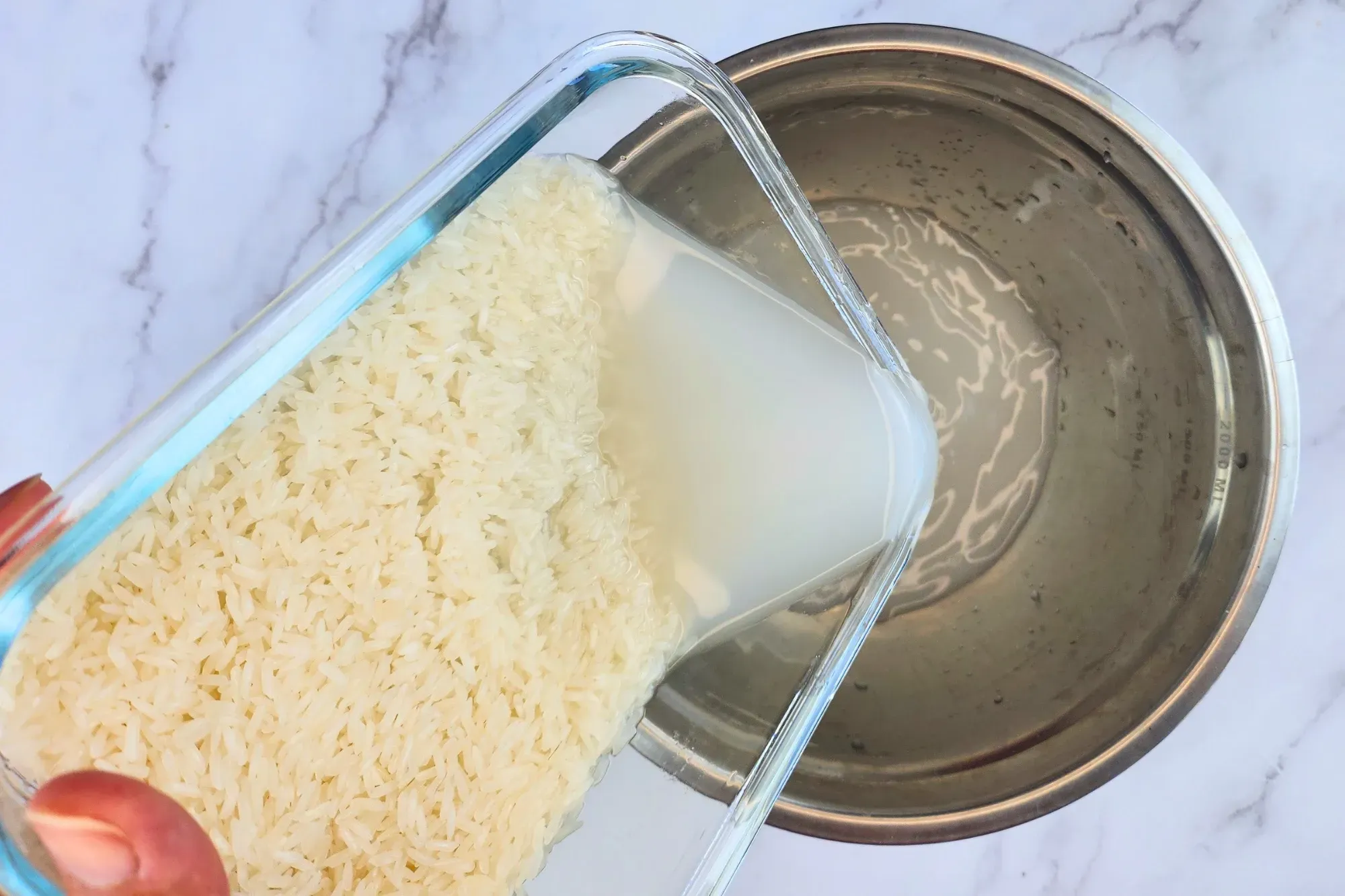 A hand rinse water out of a container of jasmine rice