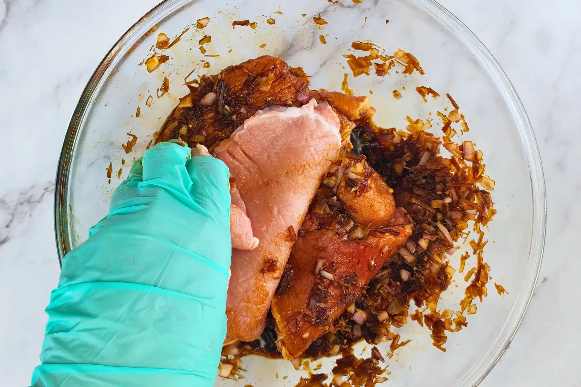 A hand rubs pork chops in a mixing bowl