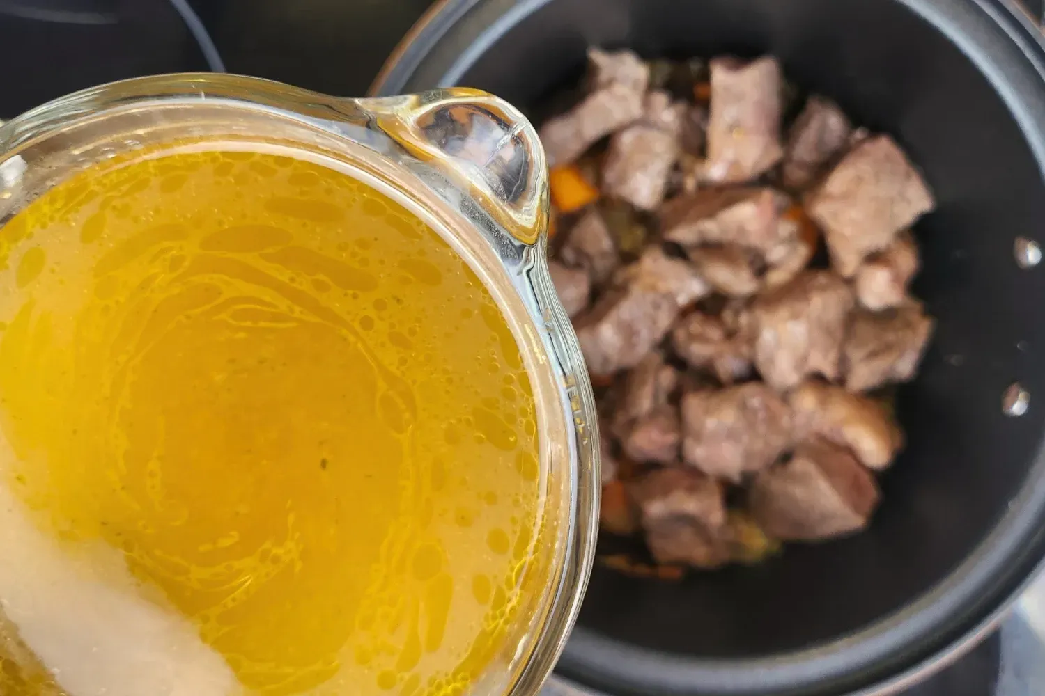 A jar of beef broth above a cooking meat pot.