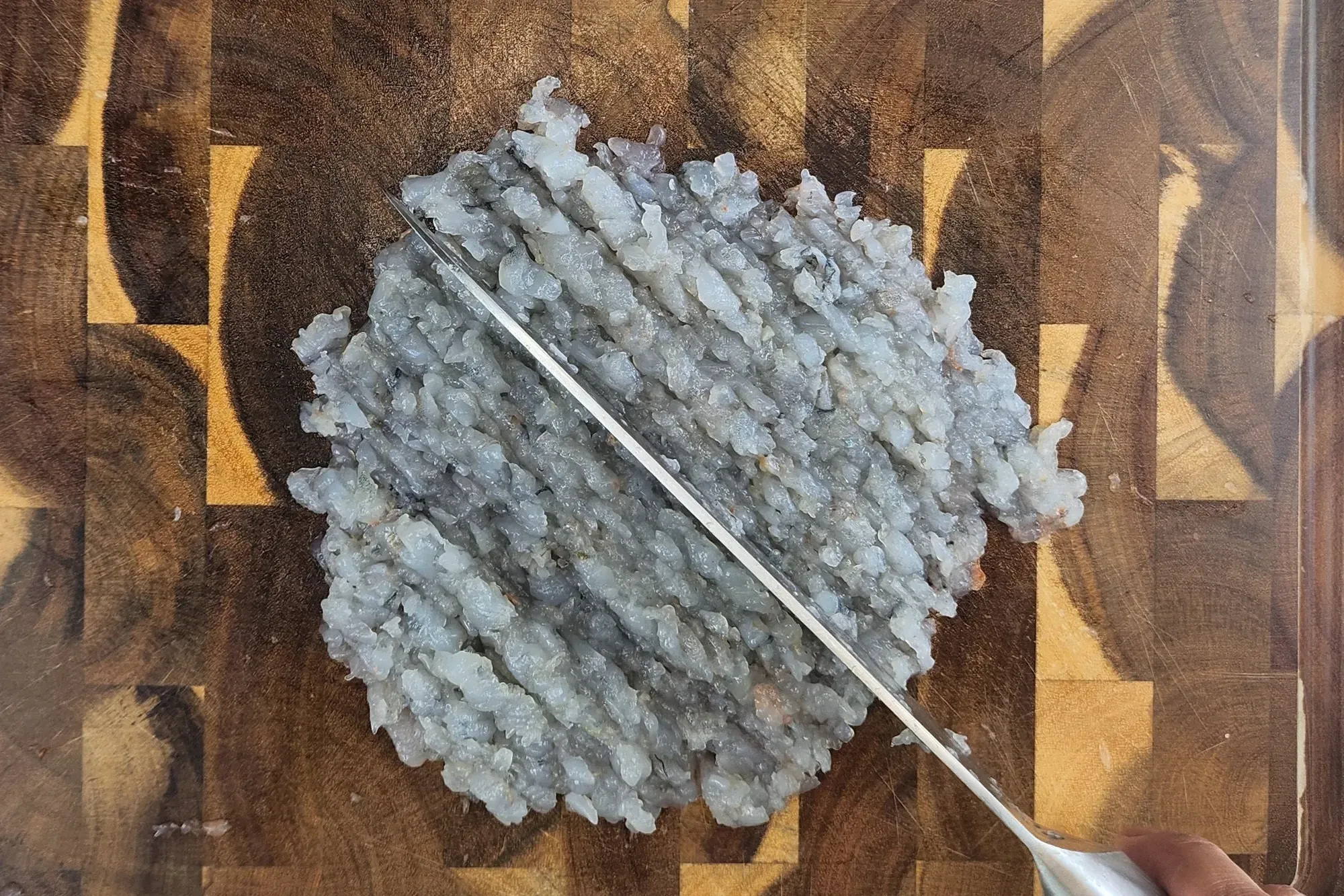 A knife is chopping raw shrimp