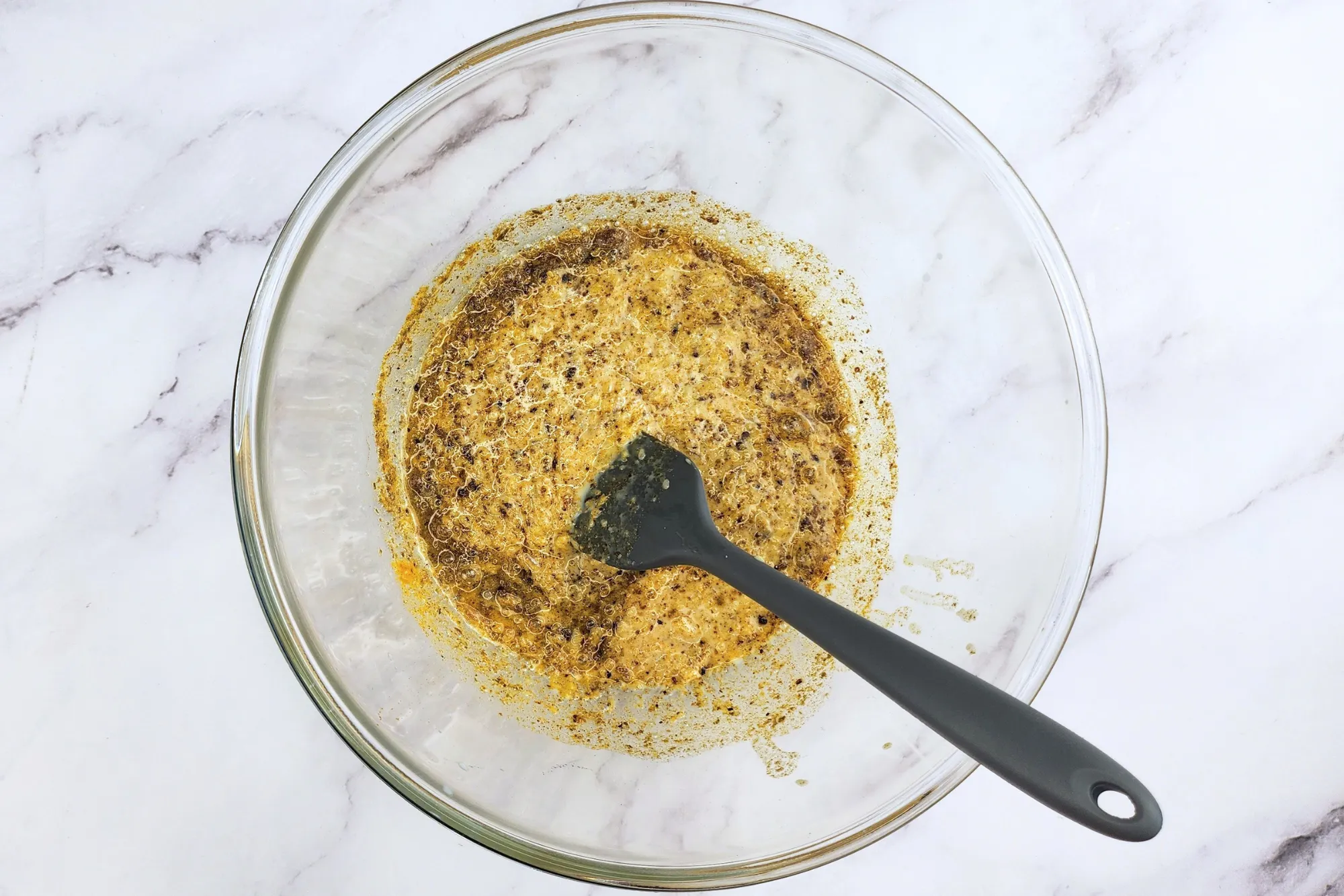 A mixing bowl with spices and spatula.