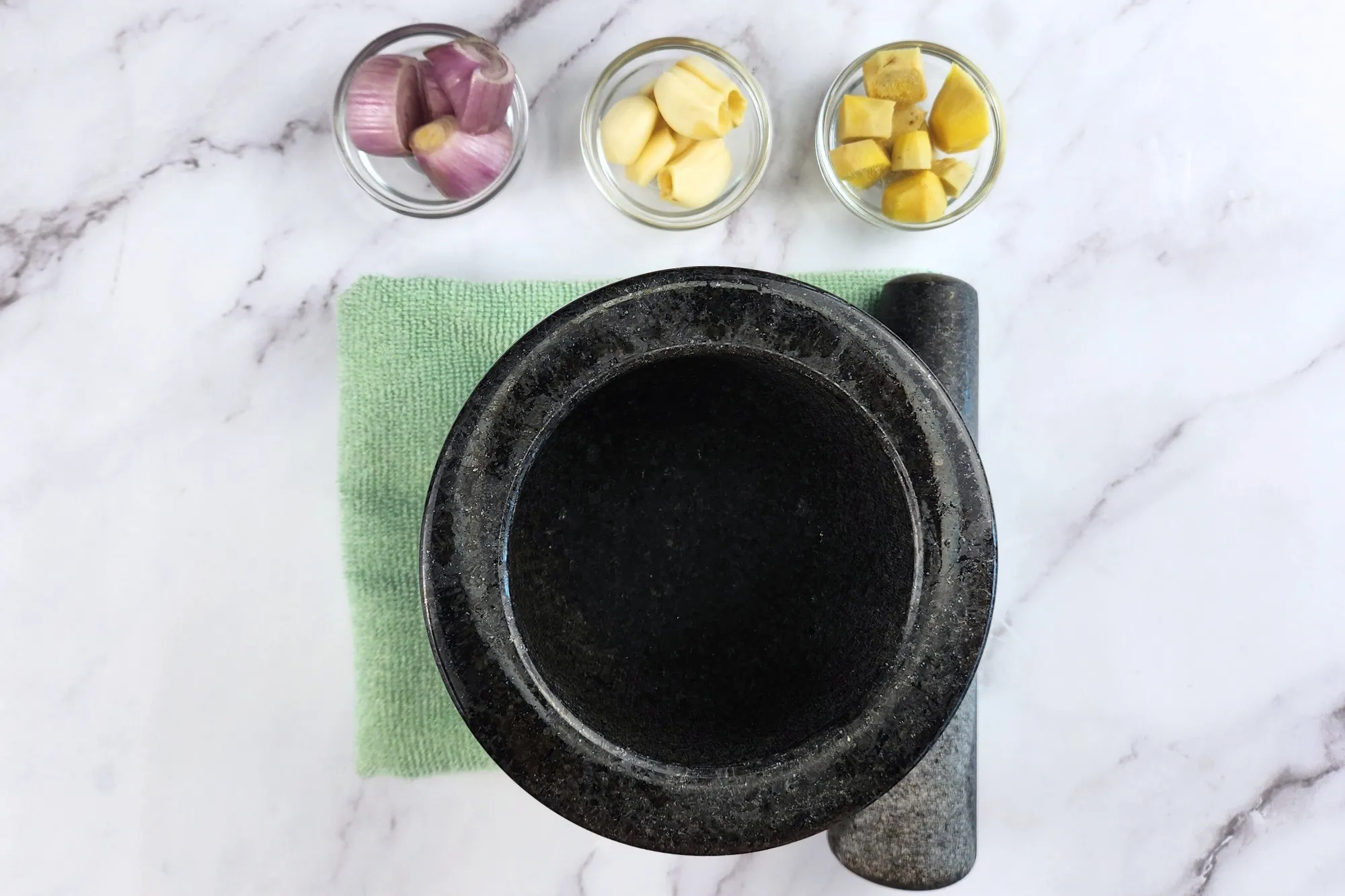A mortar with three bowl of shallots, garlic and ginger.