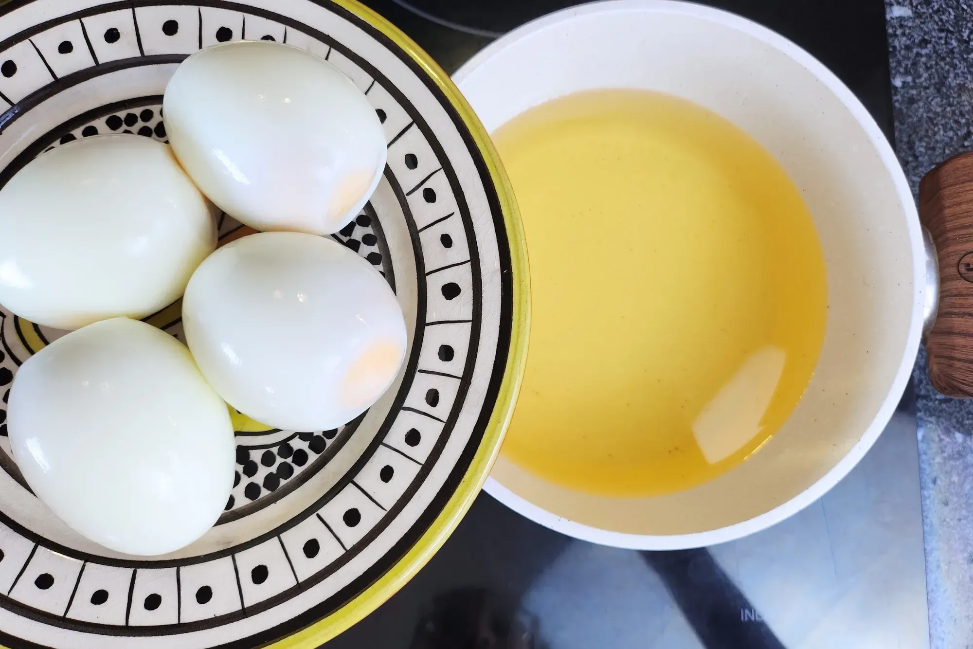 A plate of hard boiled eggs above a pot with frying oil