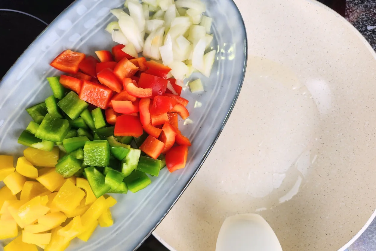 A plate of mixed bell peppers and onions above a wok.