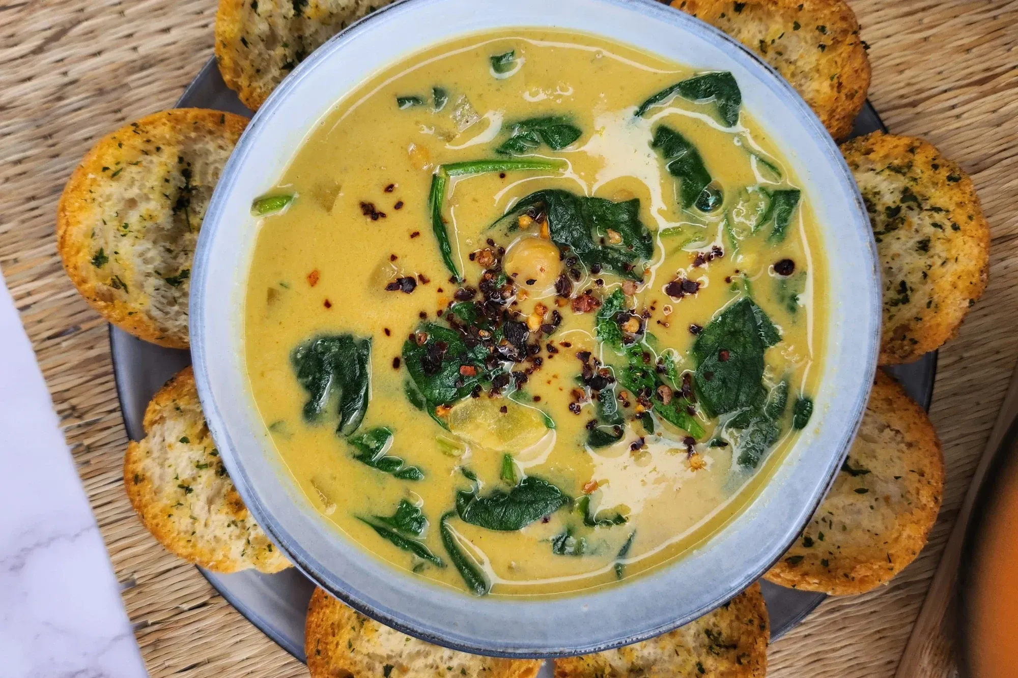 A presentation of creamy Vegan Coconut Miso Chickpea Soup with chili flakes on top and garlic breads around the bowl