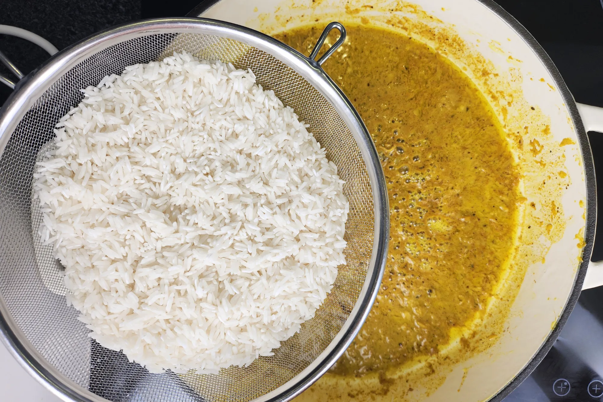 A rinsed rice is above a pan with yellow sauce.