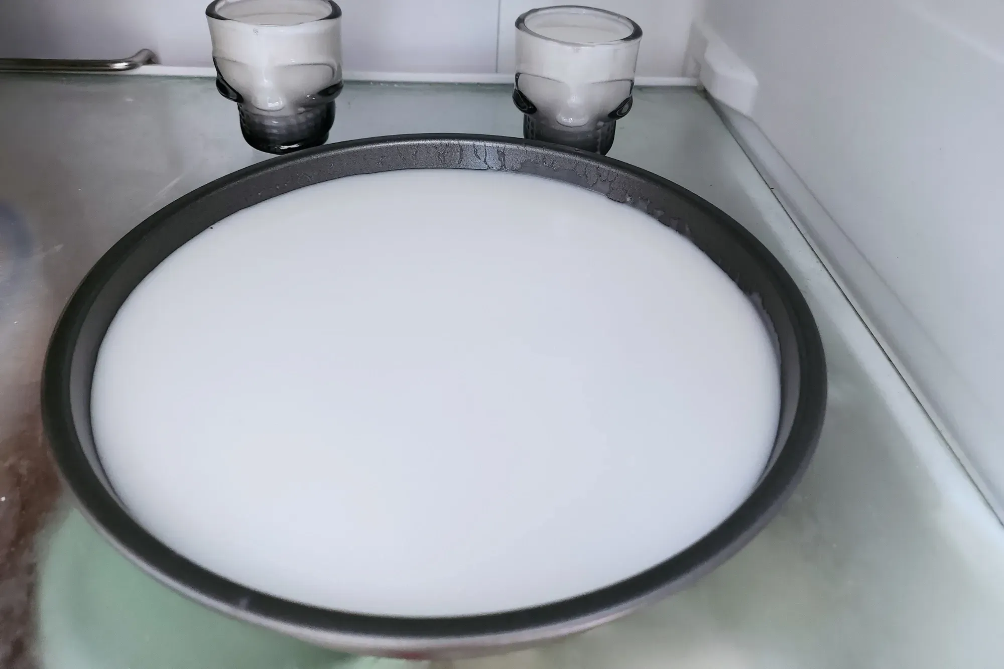 A round tray of white liquid on a chopping board next to a pot and a wooden spoon