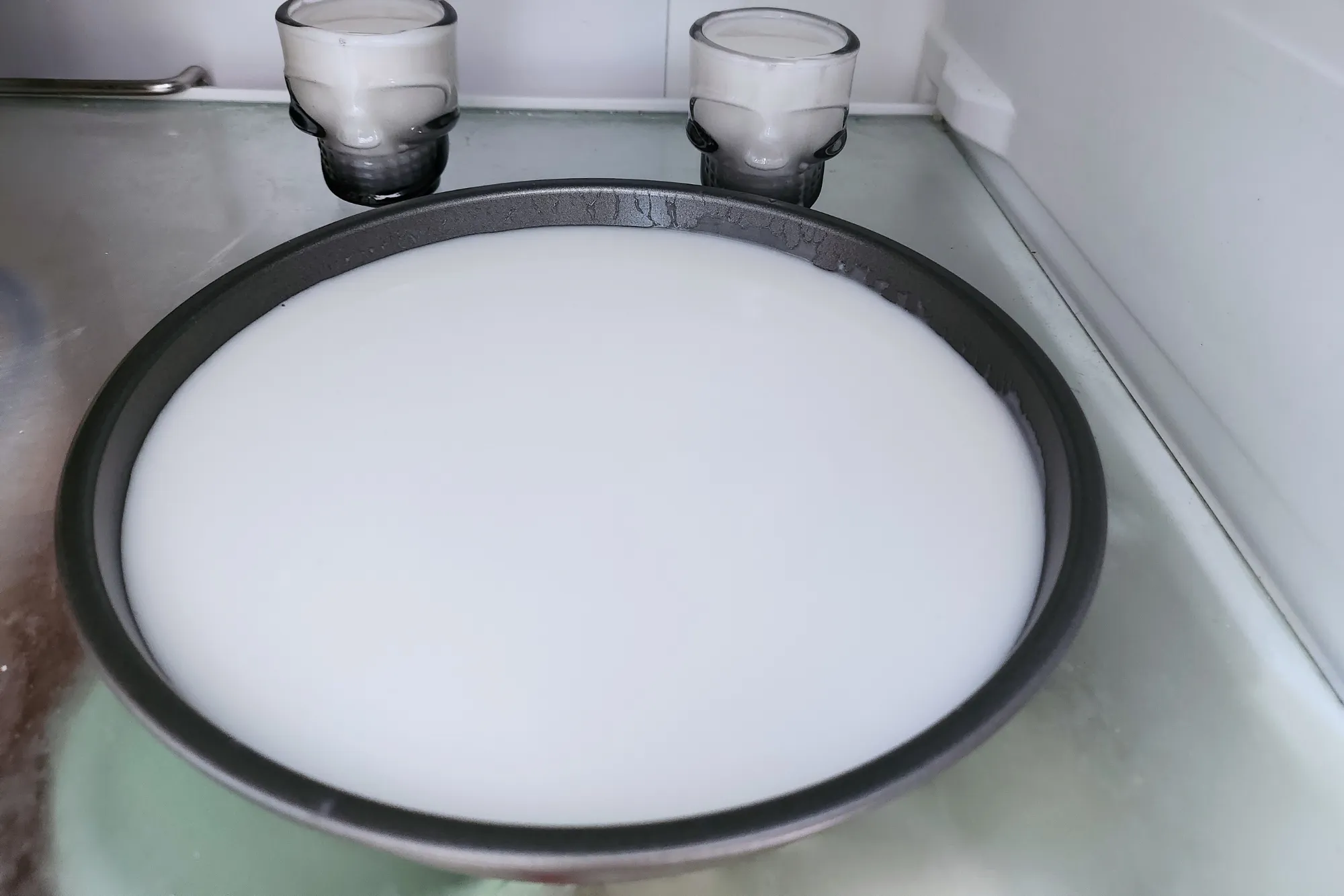 A round tray of white liquid on a chopping board next to a pot and a wooden spoon