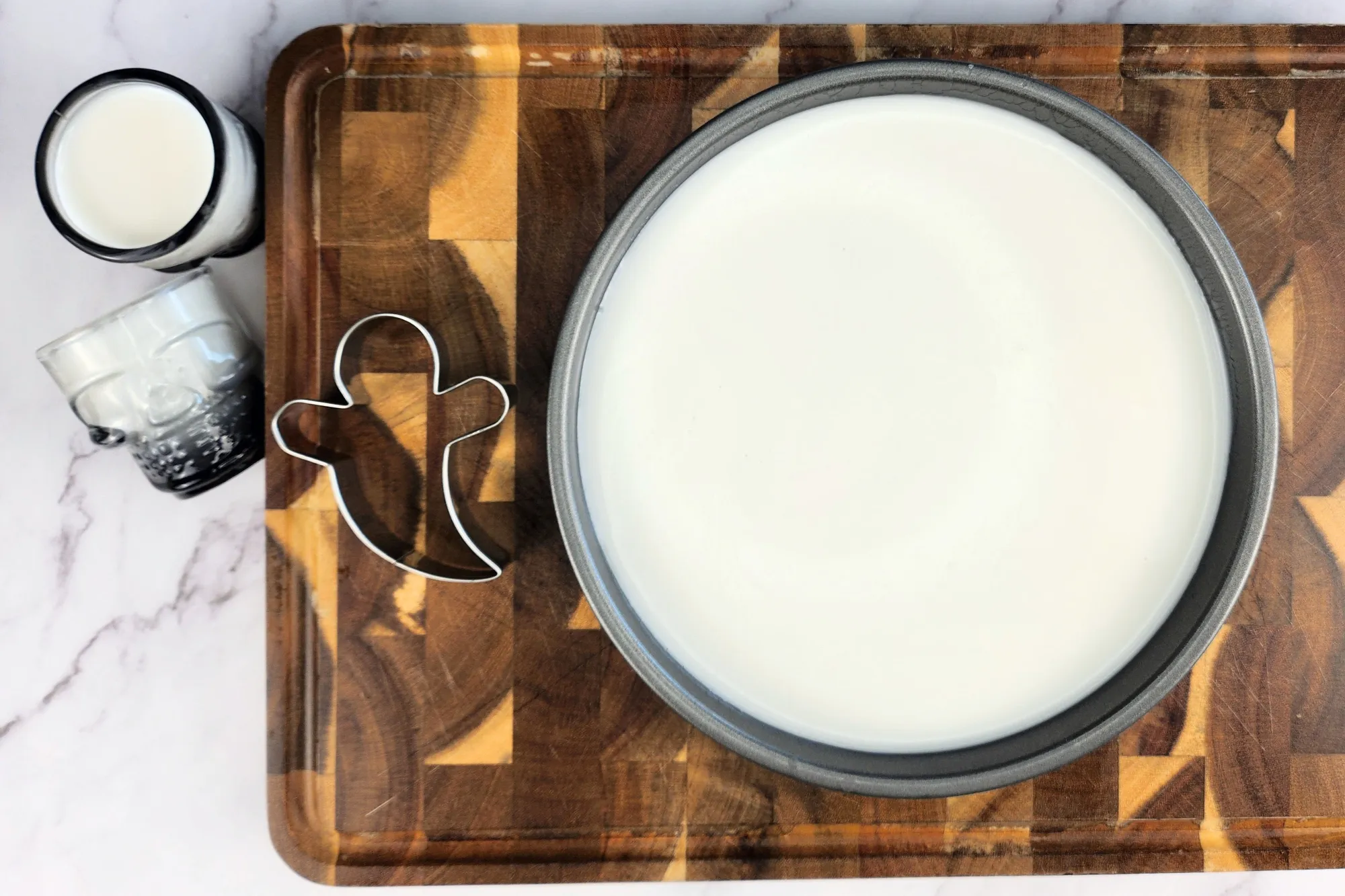 A round tray with white liquid on chopping board and a cookie cutter and two glasses shot