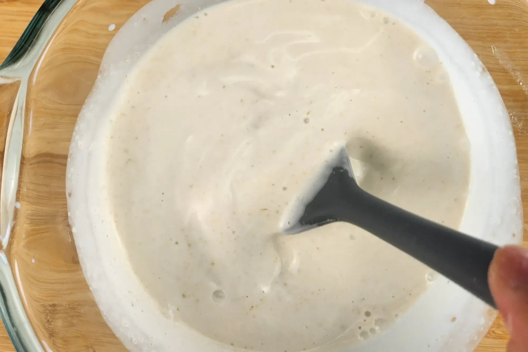 A silicone spatula is in a jar of white sauce.