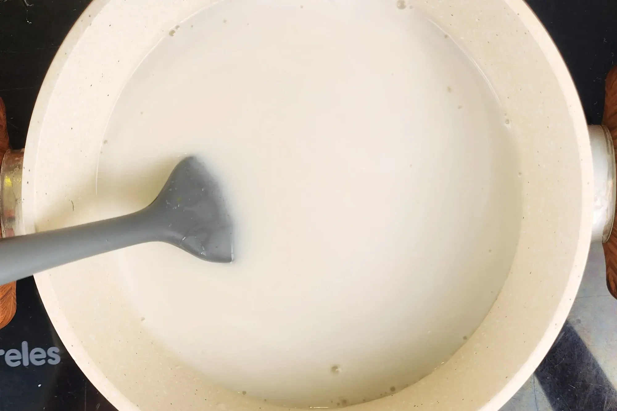 A spatula is in a pot of white liquid