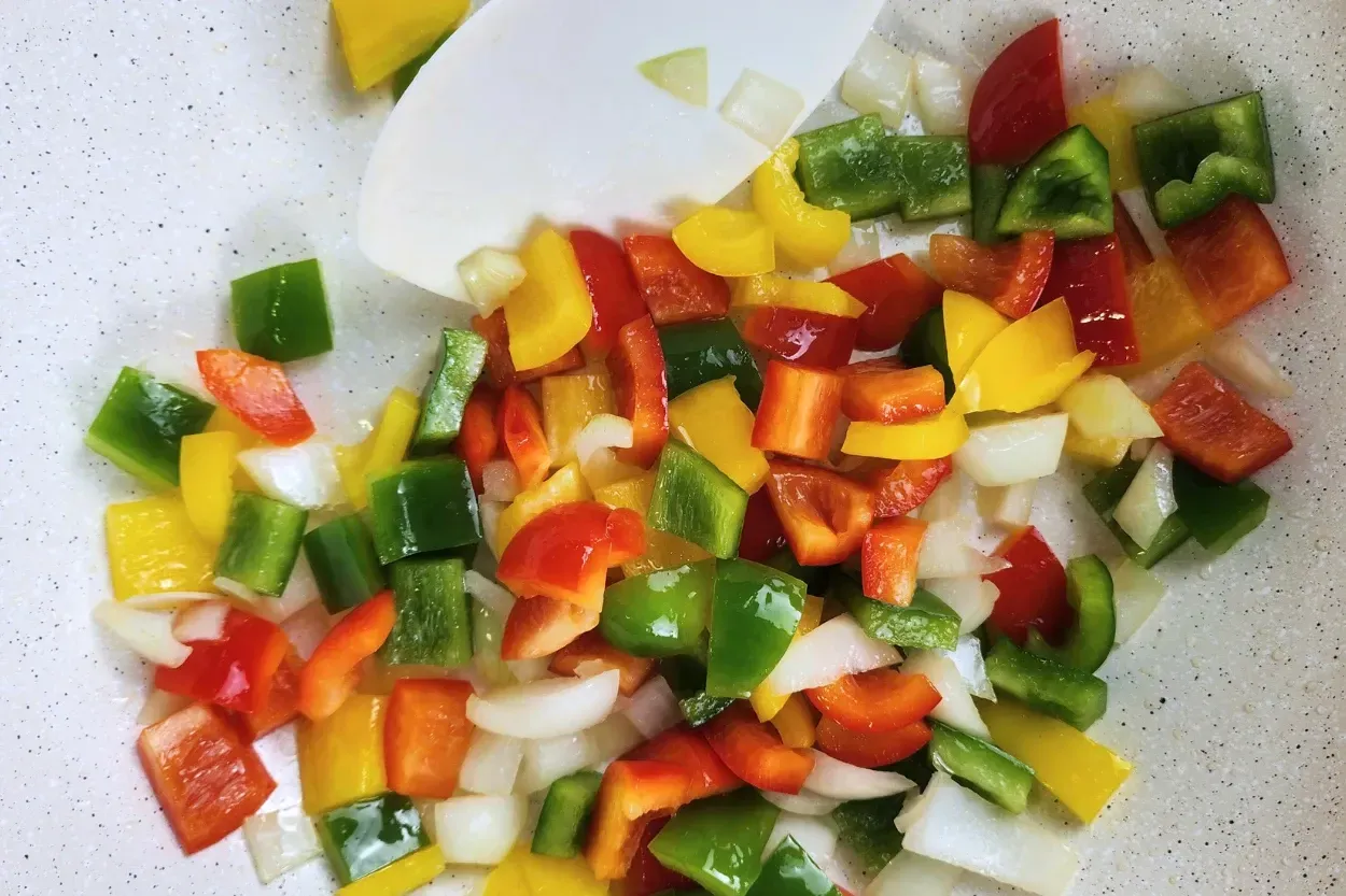 A spatula stir mixed bell peppers and onions in a wok.