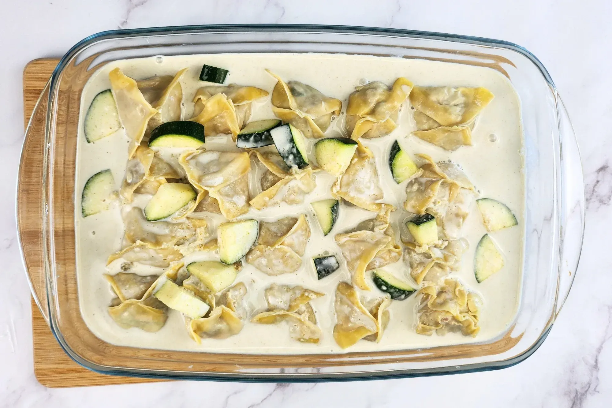 A tray of dumplings and zucchini in white sauce.