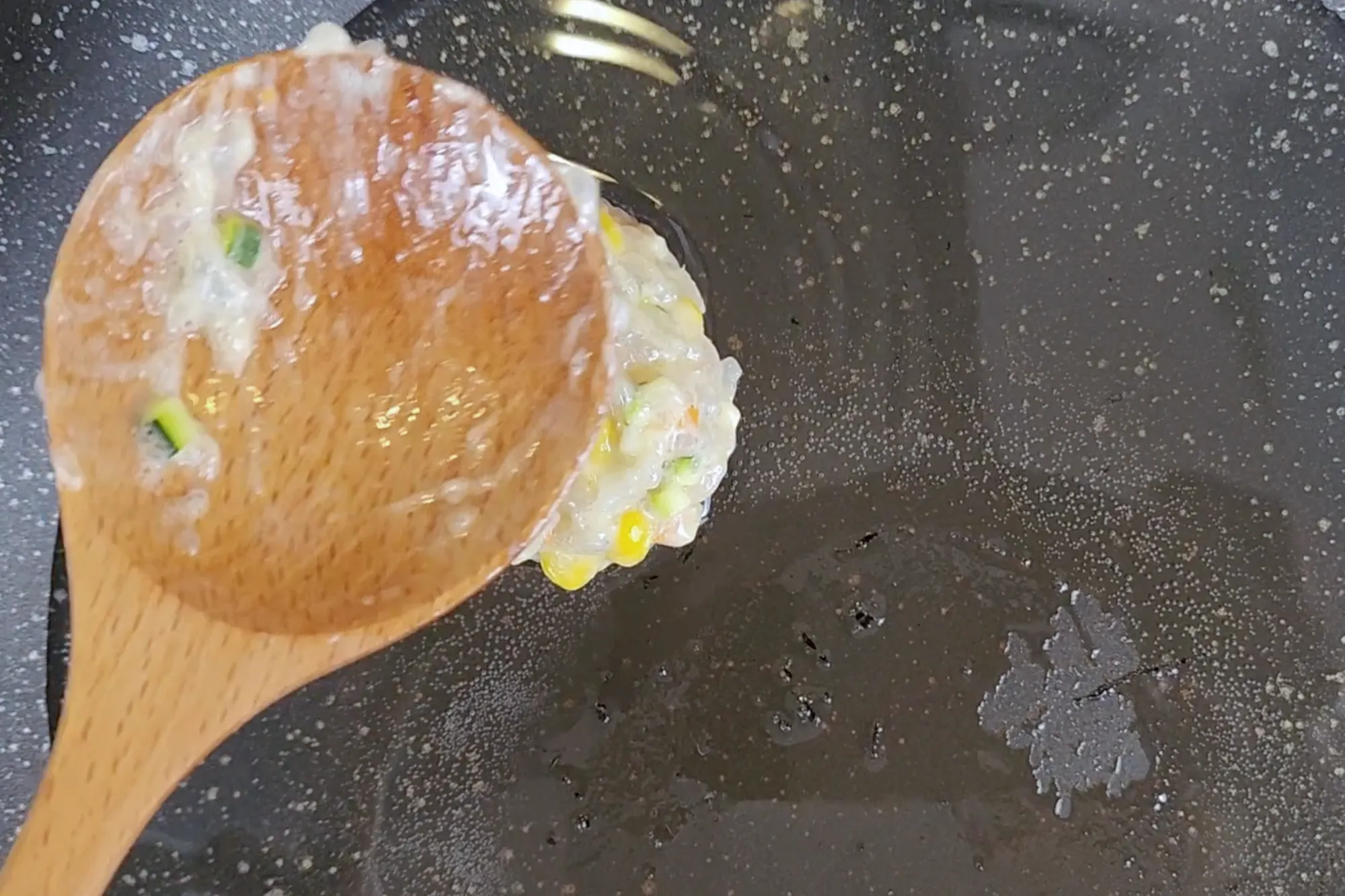 A wooden spoon above Shrimp Fritter in frying pan