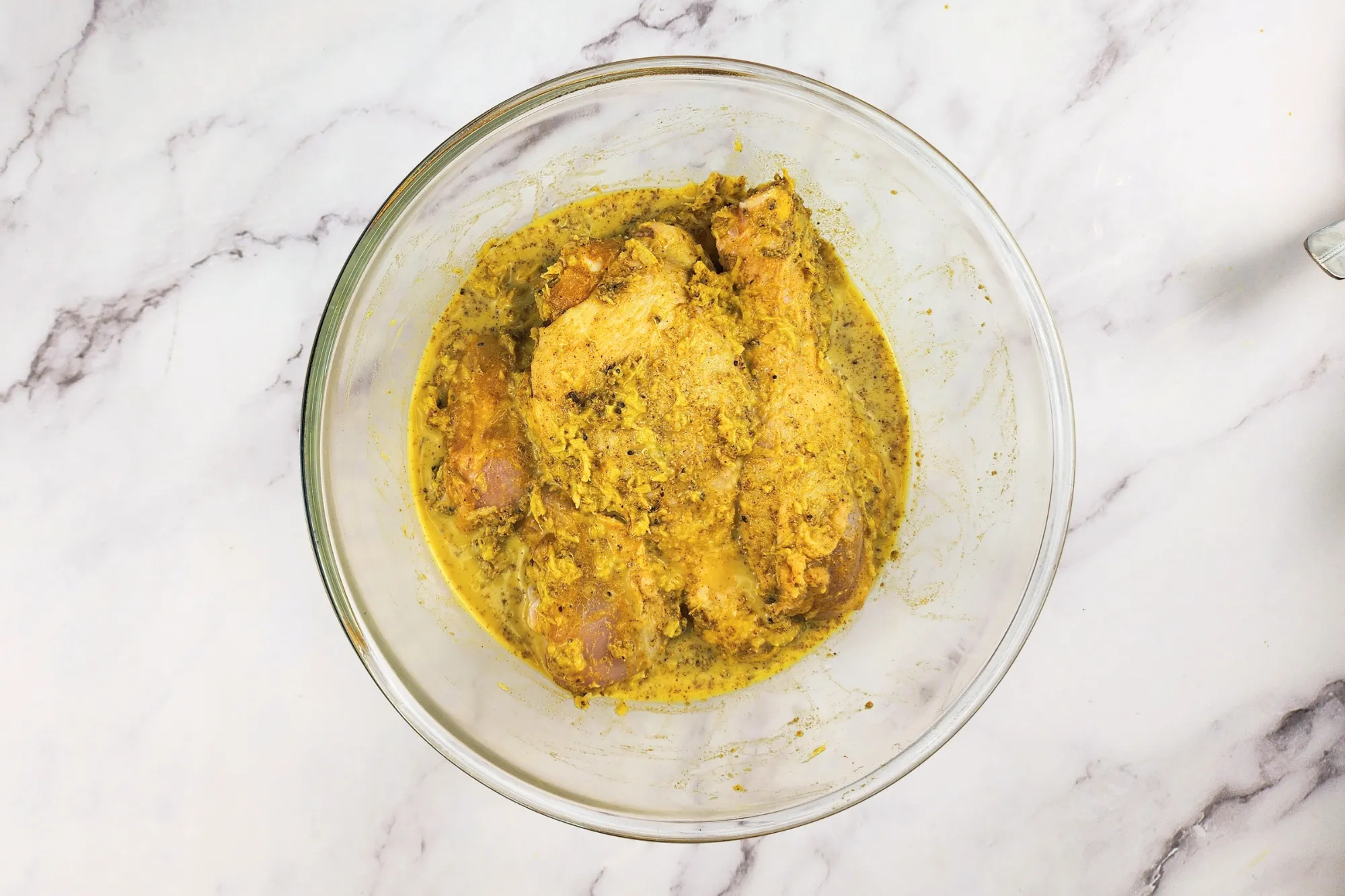Chicken drumsticks marinated with yellow sauce in a mixing bowl.