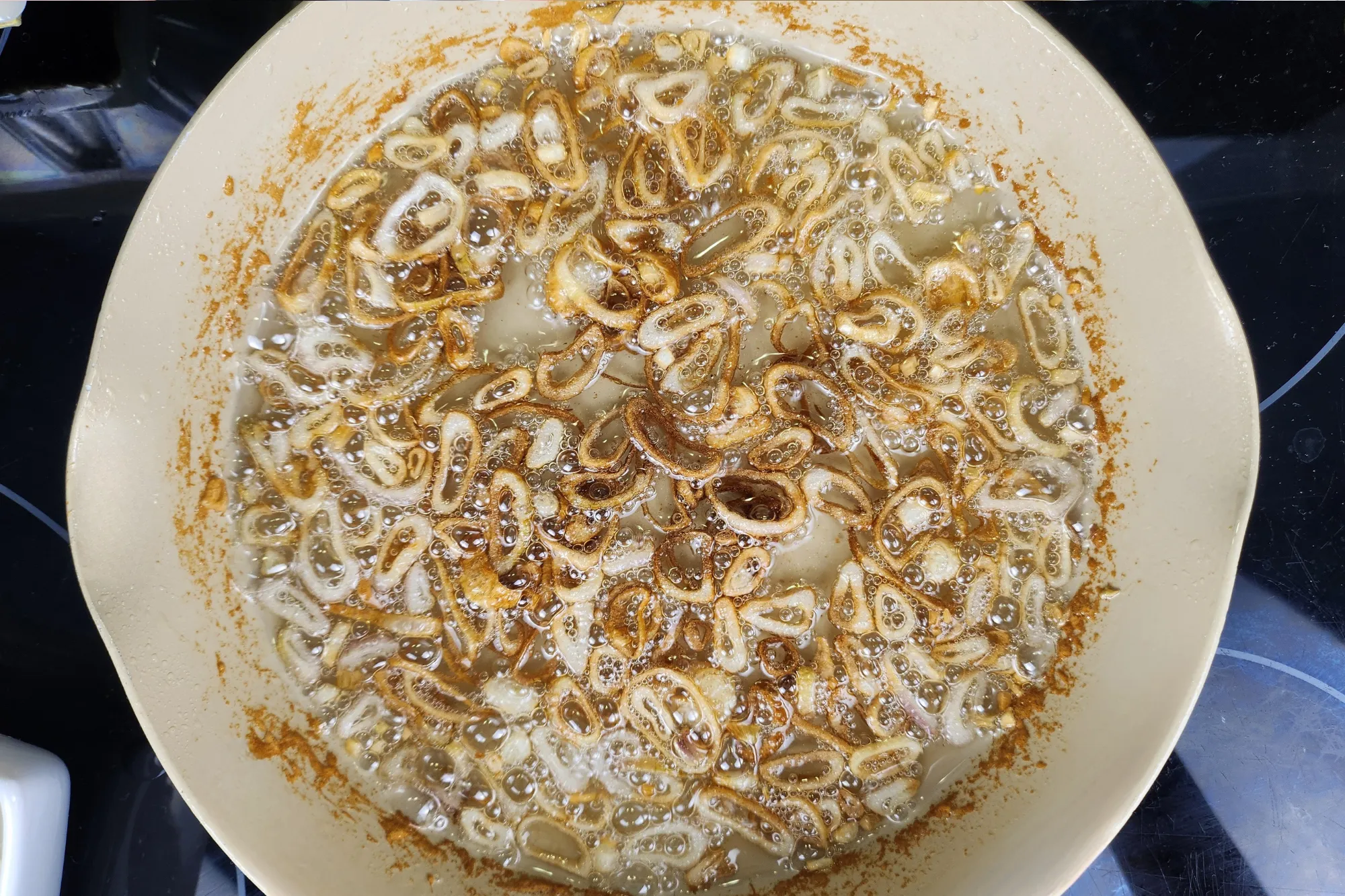 Cooked fried shallots in a small pan.