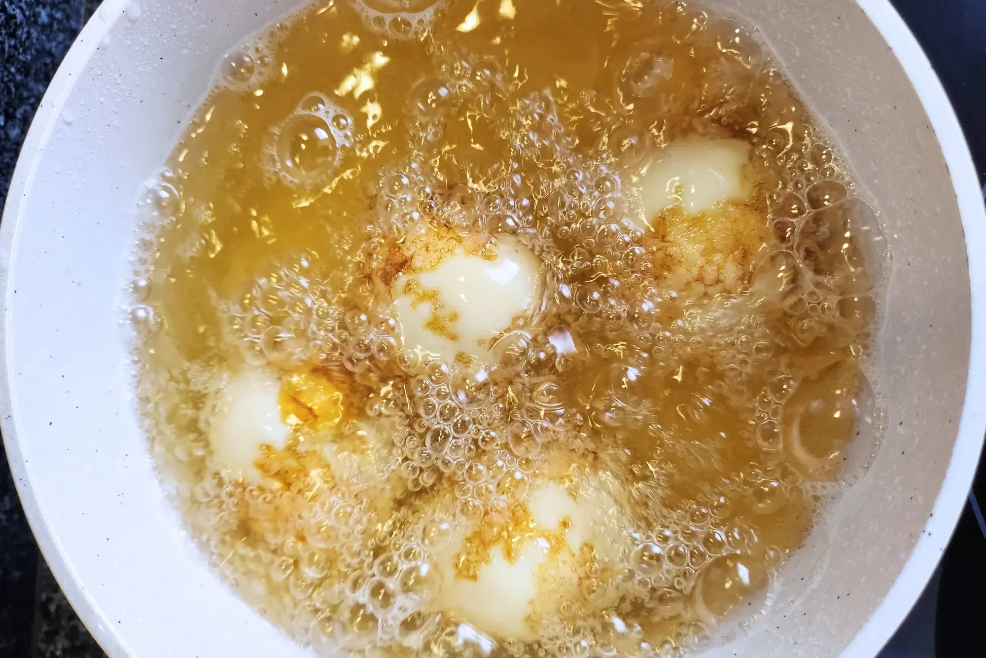 A plate of hard boiled eggs above a pot with frying oil