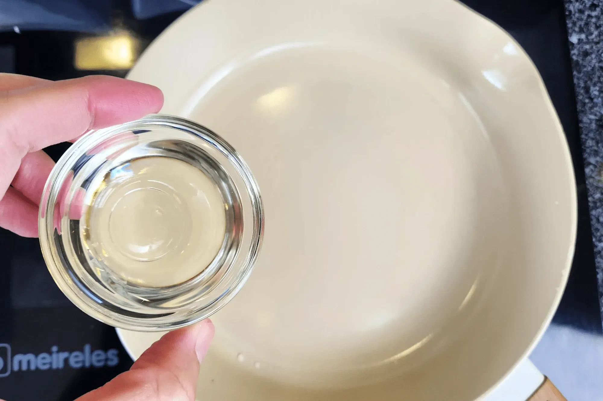 a hand holding a bowl of oil with the sauce pan