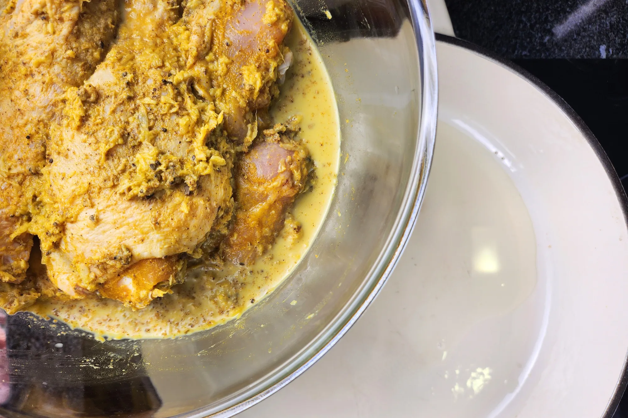 Marinated chickens in a mixing bowl is above a hot pan. 