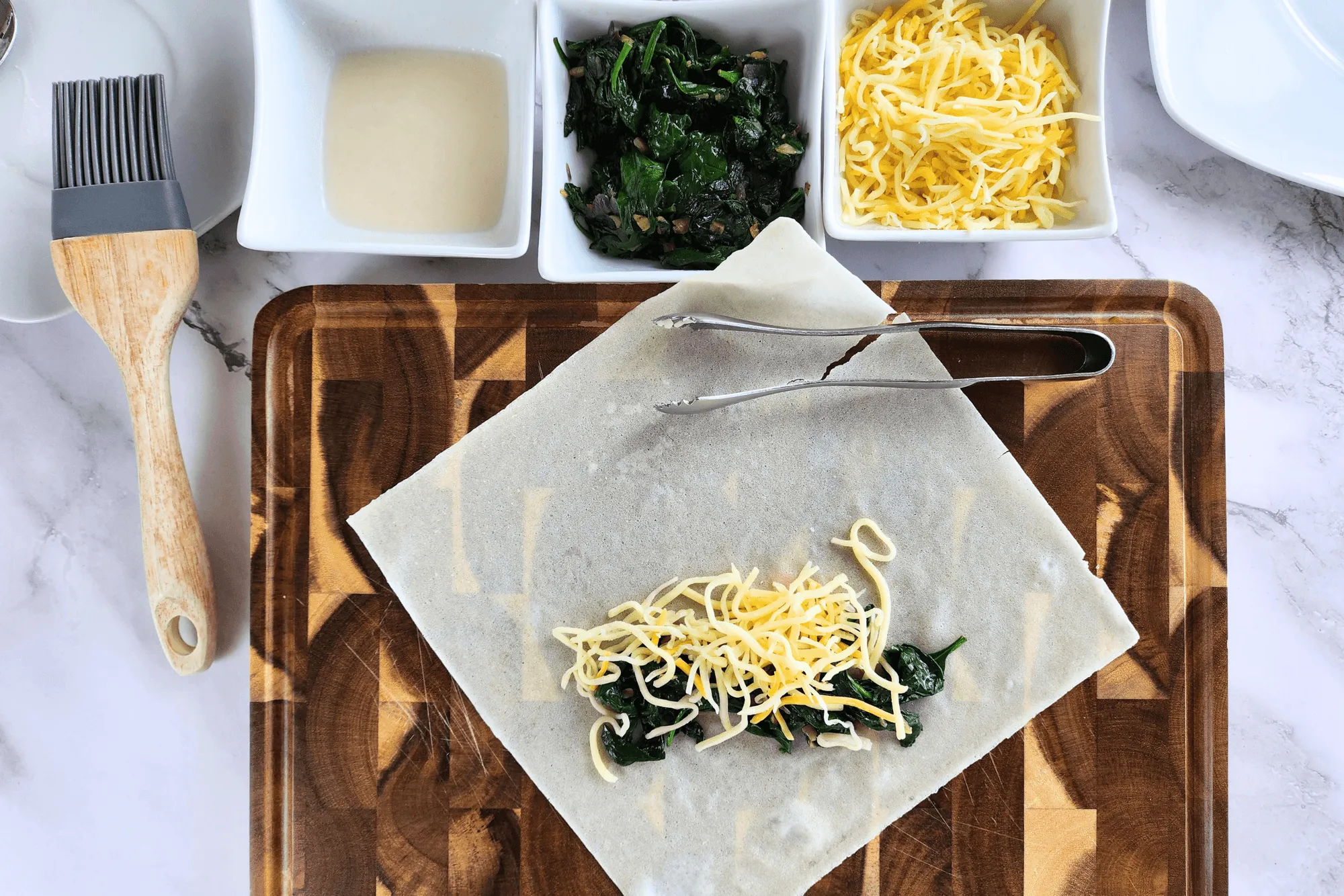 Place a spring roll wrapper on a flat surface, then add the sautéed spinach and cheese. You can adjust the amount of cheese to your liking. When rolling the wrapper, apply the flour-water mixture at the final step to seal the roll securely.