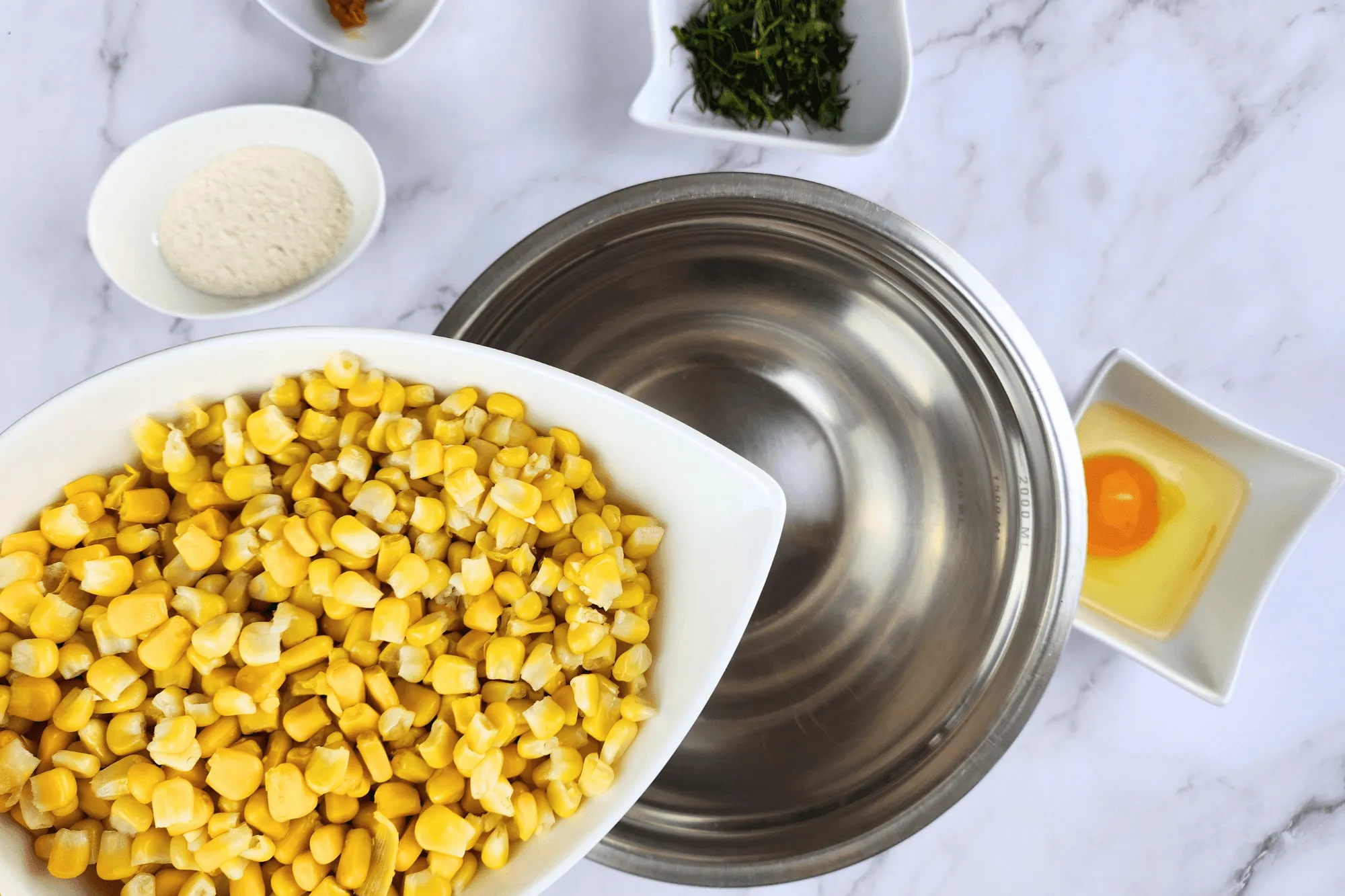 Place the cooked corn kernels in a large bowl. Season with sugar, salt, egg, red curry paste, and crispy batter flour. Add the sliced kaffir lime leaves and mix well until everything is combined.