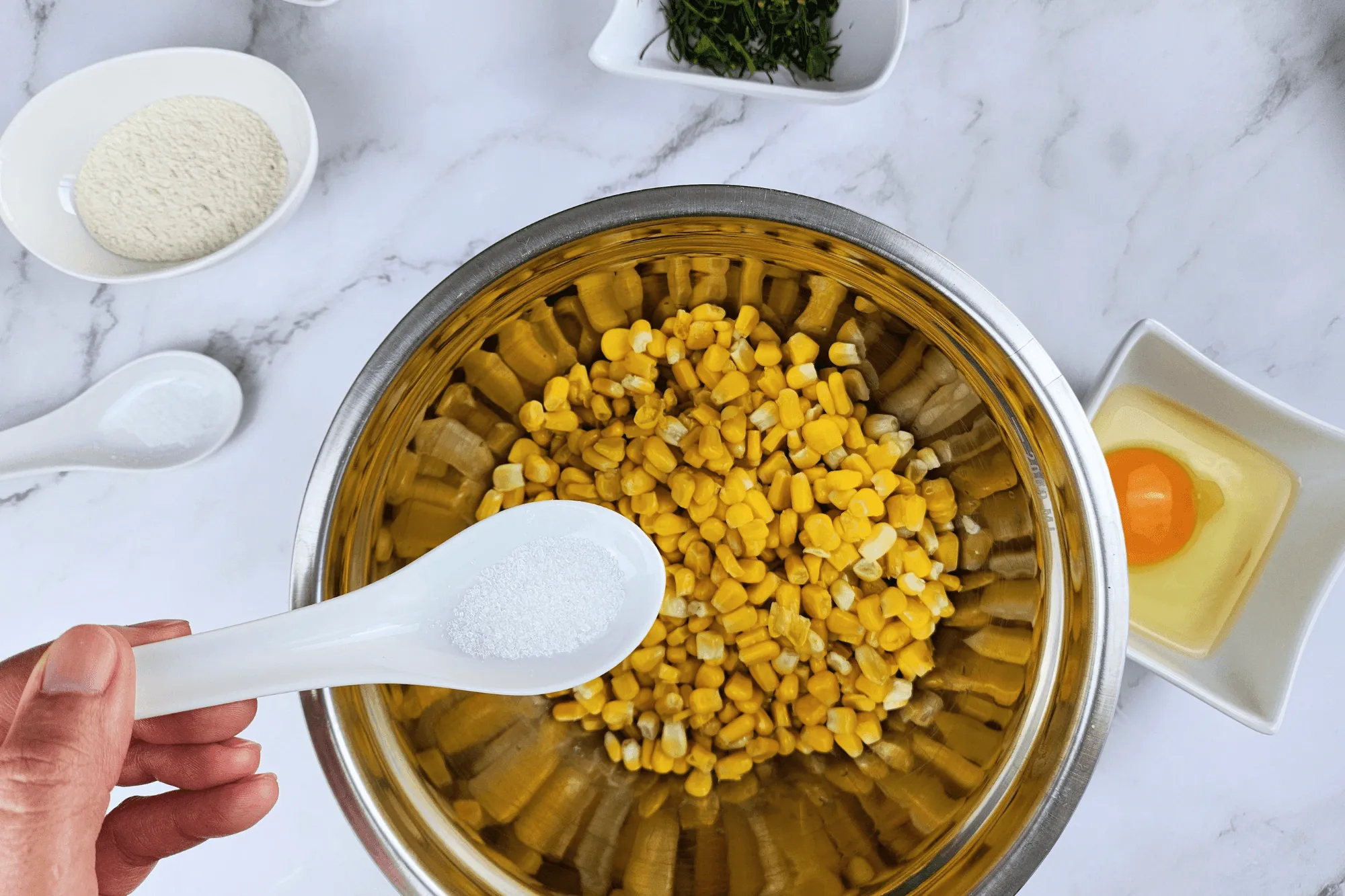 Place the cooked corn kernels in a large bowl. Season with sugar, salt, egg, red curry paste, and crispy batter flour. Add the sliced kaffir lime leaves and mix well until everything is combined.