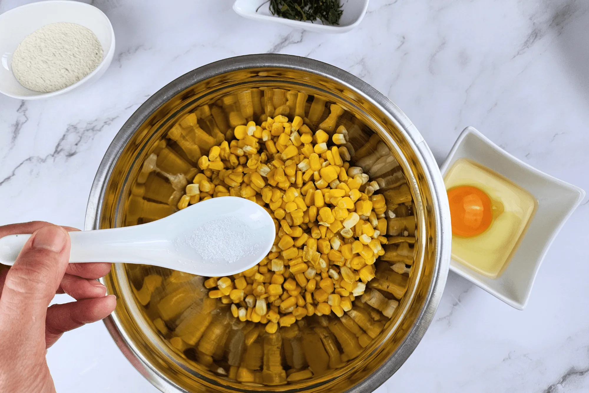 Place the cooked corn kernels in a large bowl. Season with sugar, salt, egg, red curry paste, and crispy batter flour. Add the sliced kaffir lime leaves and mix well until everything is combined.