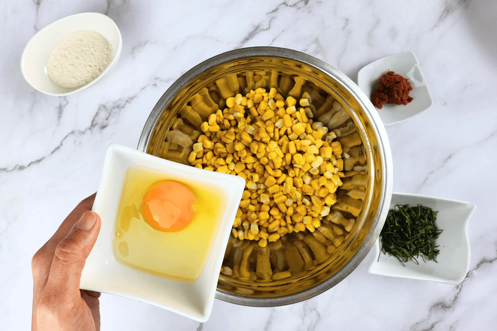 Place the cooked corn kernels in a large bowl. Season with sugar, salt, egg, red curry paste, and crispy batter flour. Add the sliced kaffir lime leaves and mix well until everything is combined.