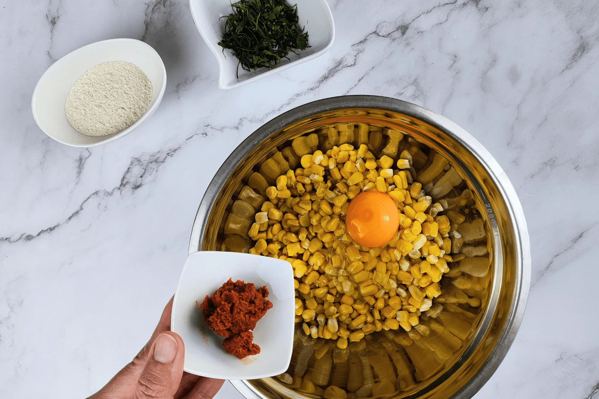 Place the cooked corn kernels in a large bowl. Season with sugar, salt, egg, red curry paste, and crispy batter flour. Add the sliced kaffir lime leaves and mix well until everything is combined.