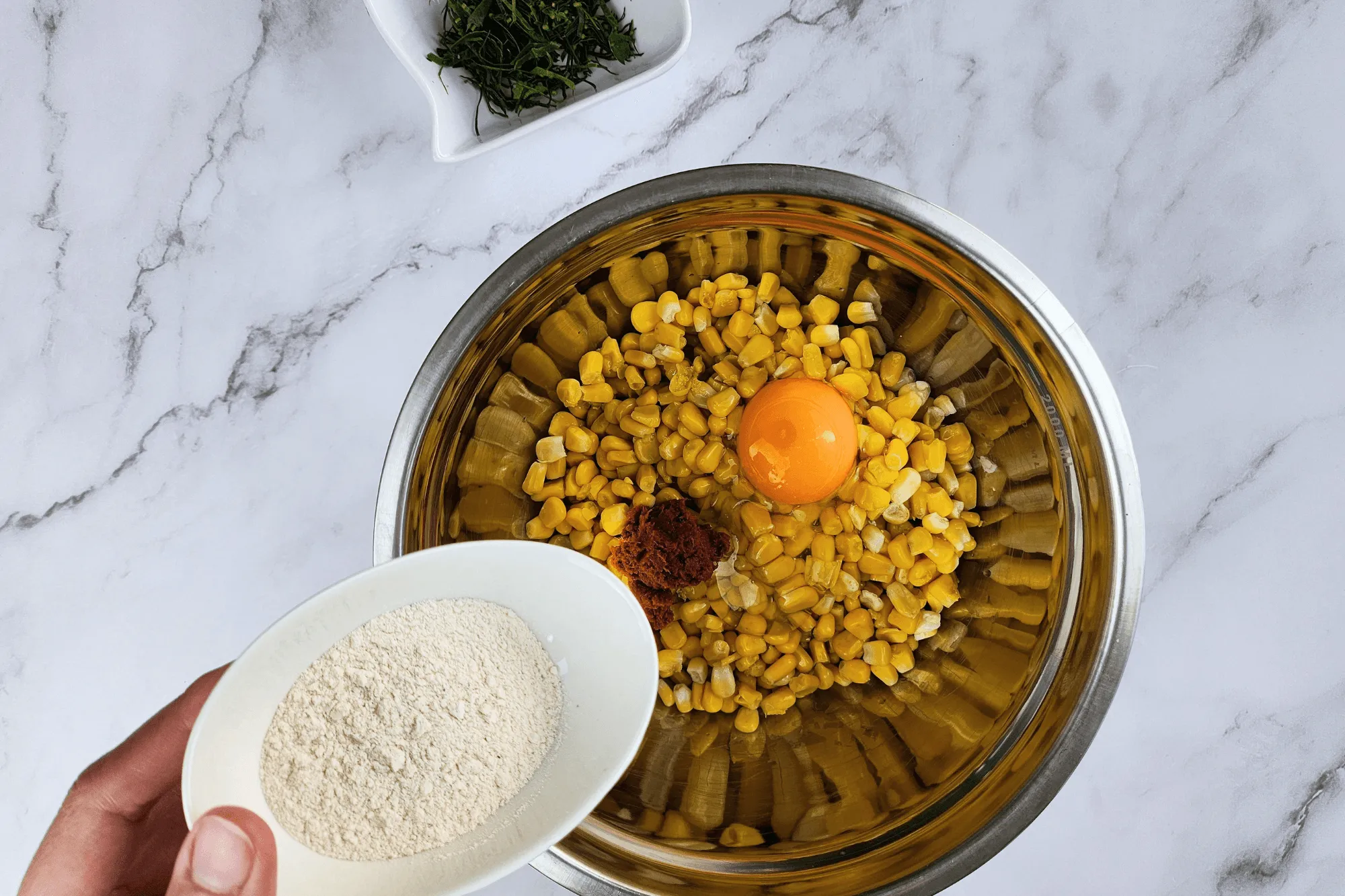 Place the cooked corn kernels in a large bowl. Season with sugar, salt, egg, red curry paste, and crispy batter flour. Add the sliced kaffir lime leaves and mix well until everything is combined.