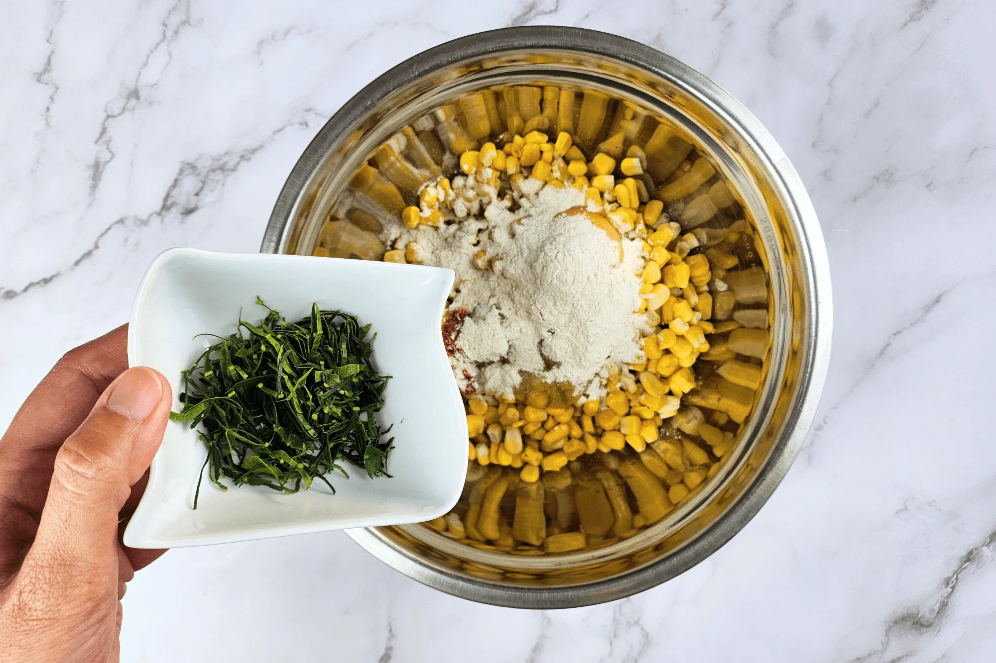 Place the cooked corn kernels in a large bowl. Season with sugar, salt, egg, red curry paste, and crispy batter flour. Add the sliced kaffir lime leaves and mix well until everything is combined.