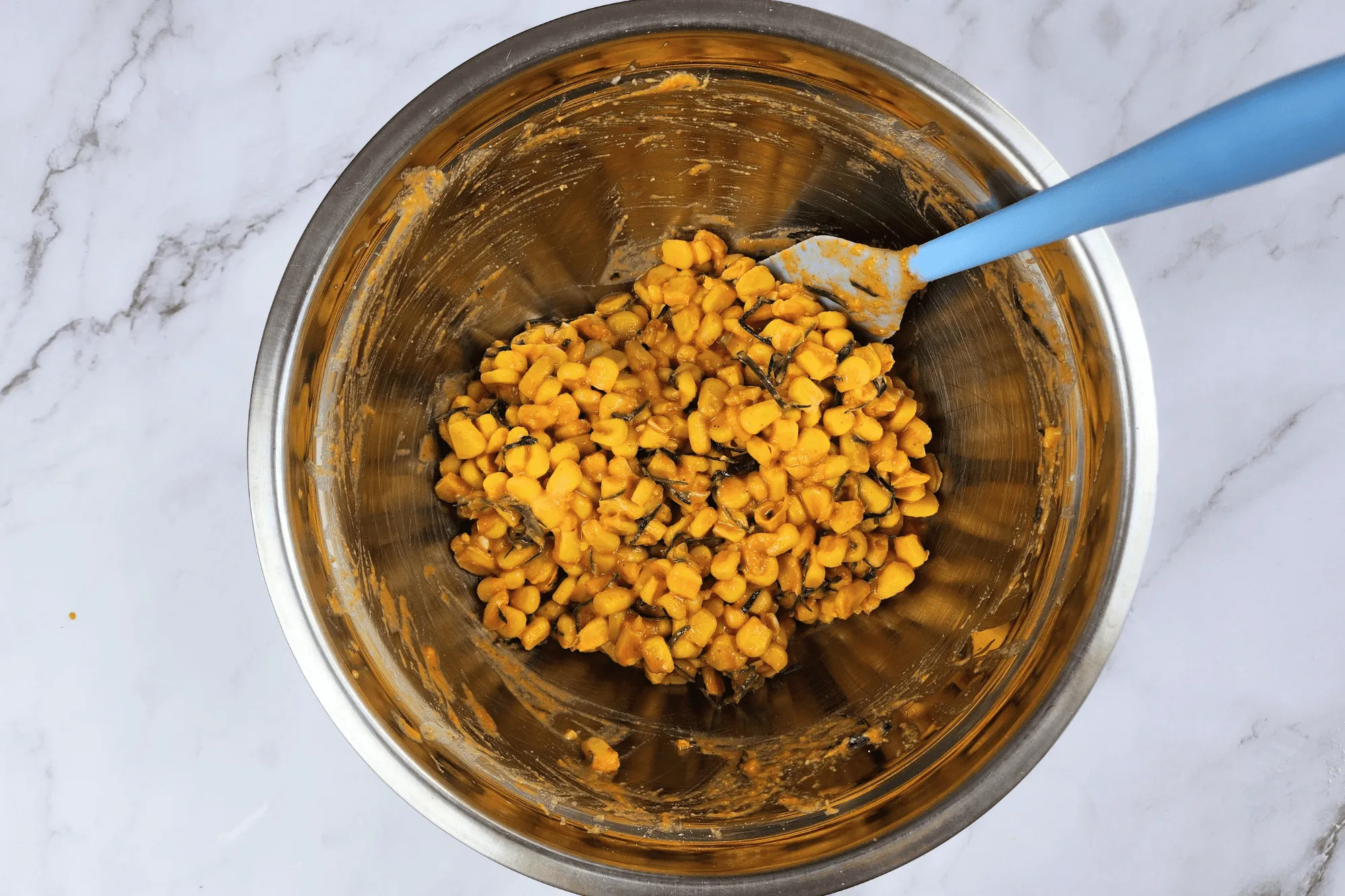 Place the cooked corn kernels in a large bowl. Season with sugar, salt, egg, red curry paste, and crispy batter flour. Add the sliced kaffir lime leaves and mix well until everything is combined.