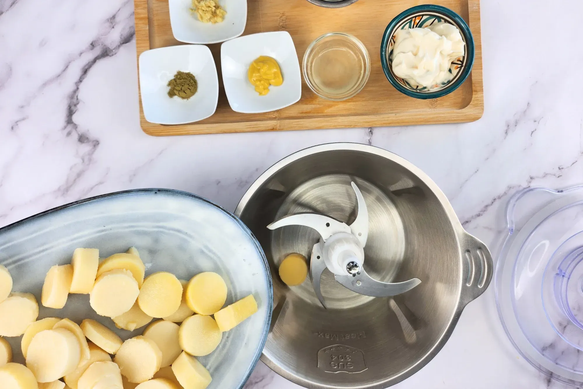 Sliced hearts of palm are being poured from a gray-blue plate into a food processor bowl with sharp blades. 
